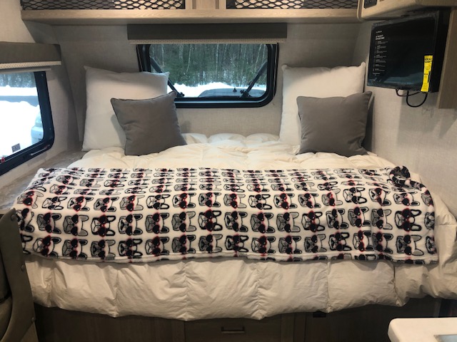Cozy RV rental bedroom featuring a white comforter, grey pillows, and a French Bulldog blanket, with a snowy outdoor view.. Forest River Rockwood Geo Pro 2021