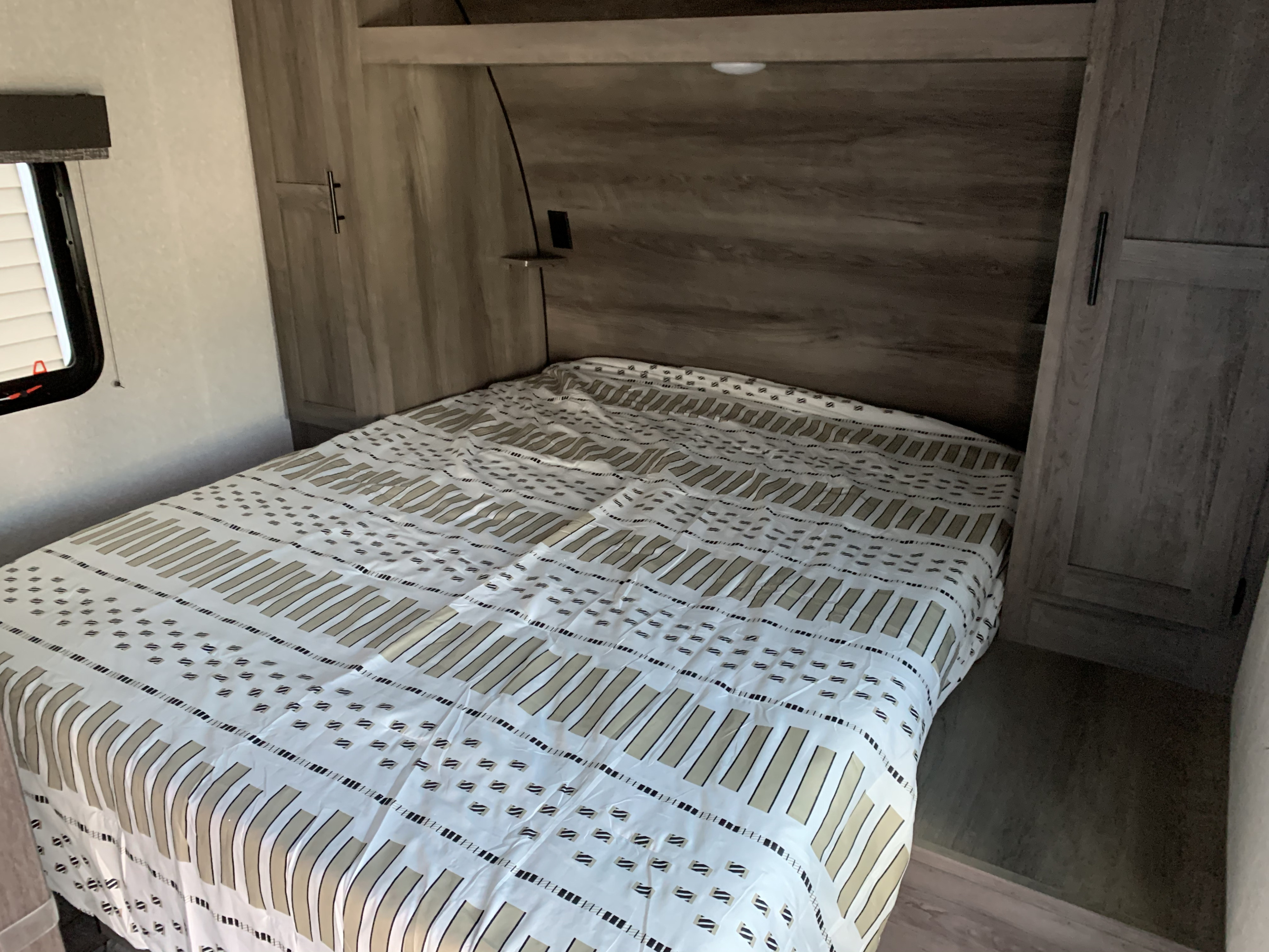 View of an RV rental bedroom: bed with patterned comforter, built-in cabinets, and window with blinds.. K-Z Manufacturing Sportsmen 2021