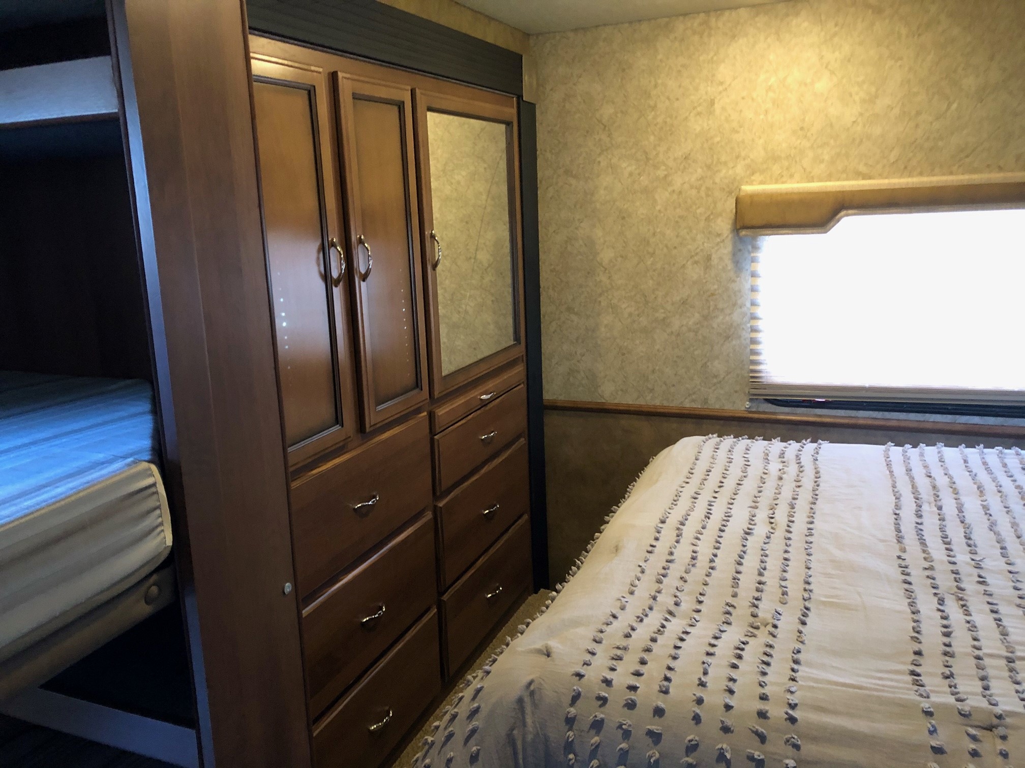 RV rental bedroom with bunk beds, central storage unit, and main bed by window. Practical and organized interior for travel.. Jamboree Sport 2014