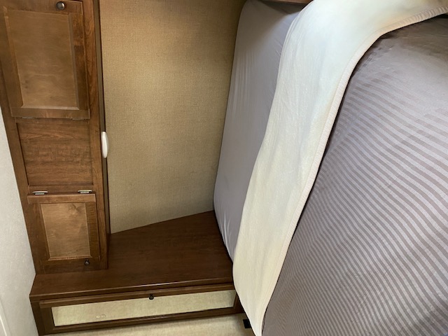 Compact RV rental bedroom with a striped bed and wooden built-in cabinet storage.. Keystone Hideout 2017