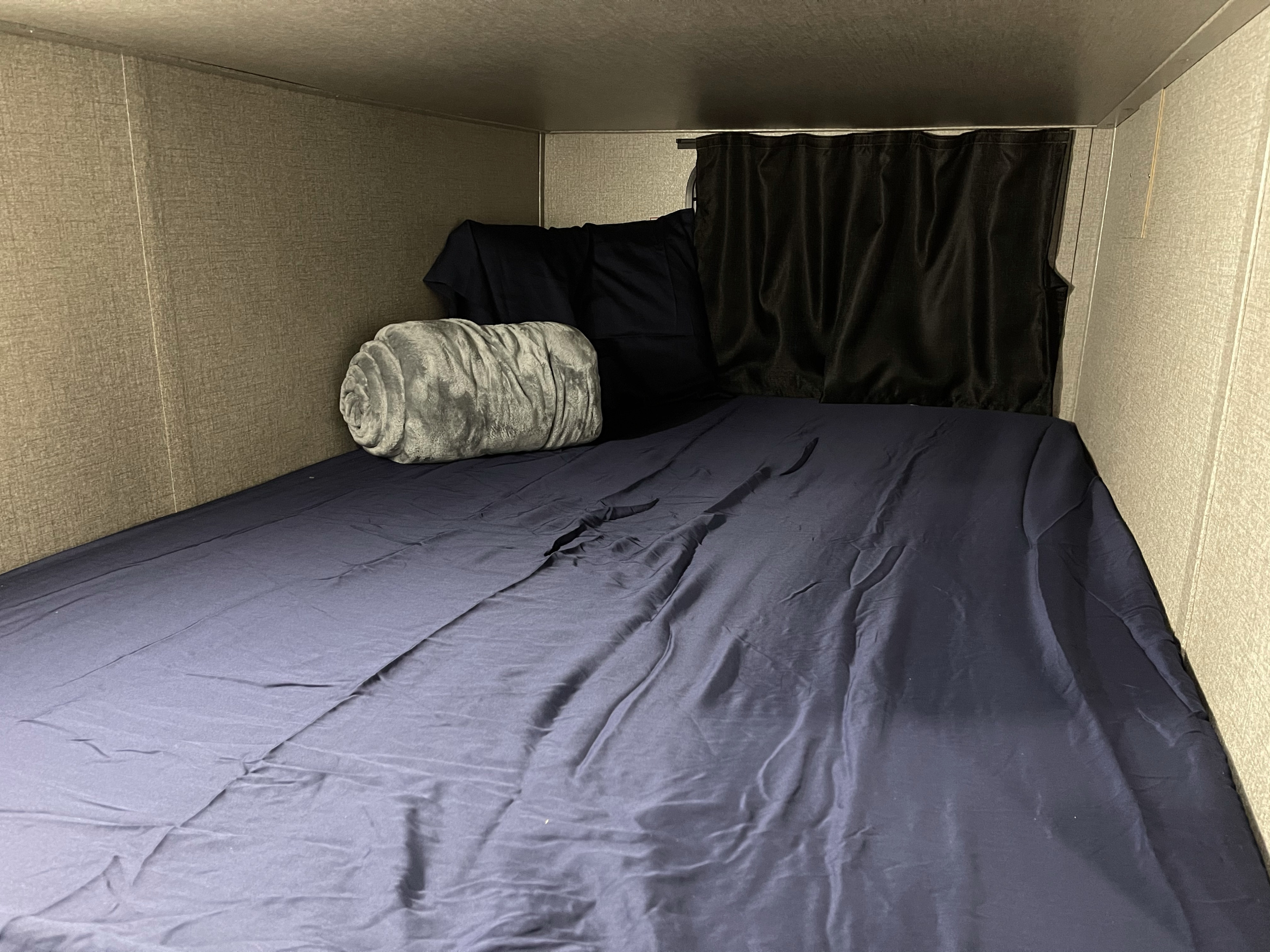 A compact sleeping area inside an RV rental, featuring a navy bunk bed with a grey blanket and privacy curtain.. Jayco Jay Flight 2021