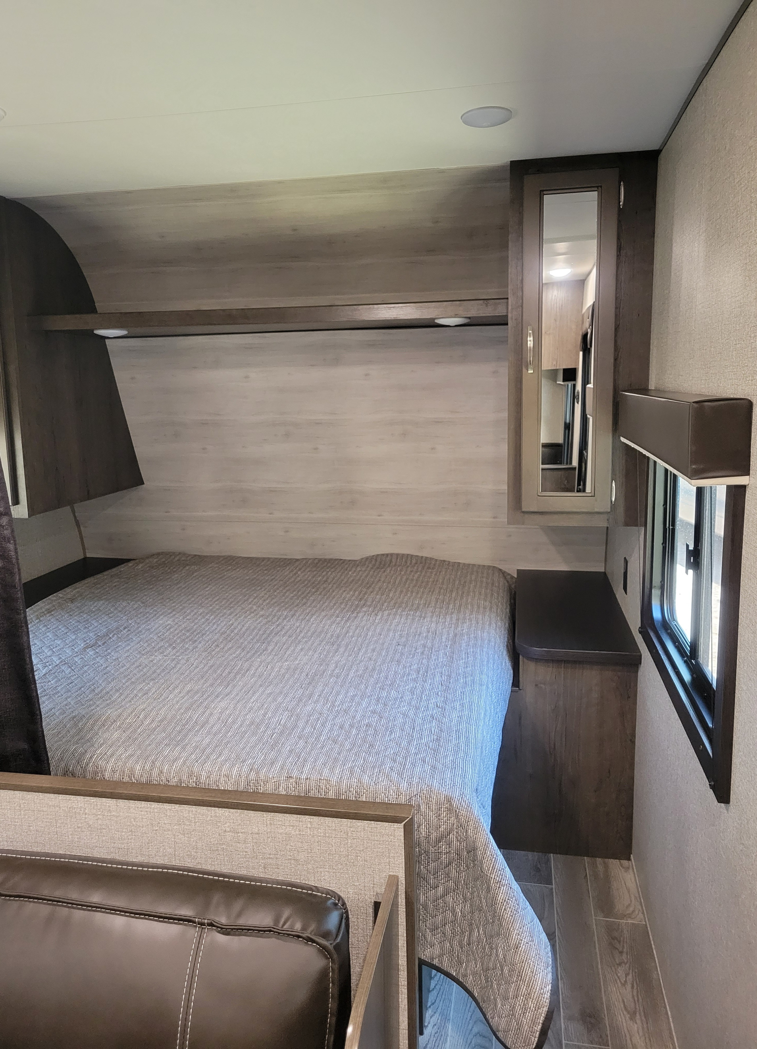 Compact RV rental bedroom featuring a bed with patterned cover, dark wood-look cabinetry, and efficient storage solutions.. Jayco Jay Flight 2021