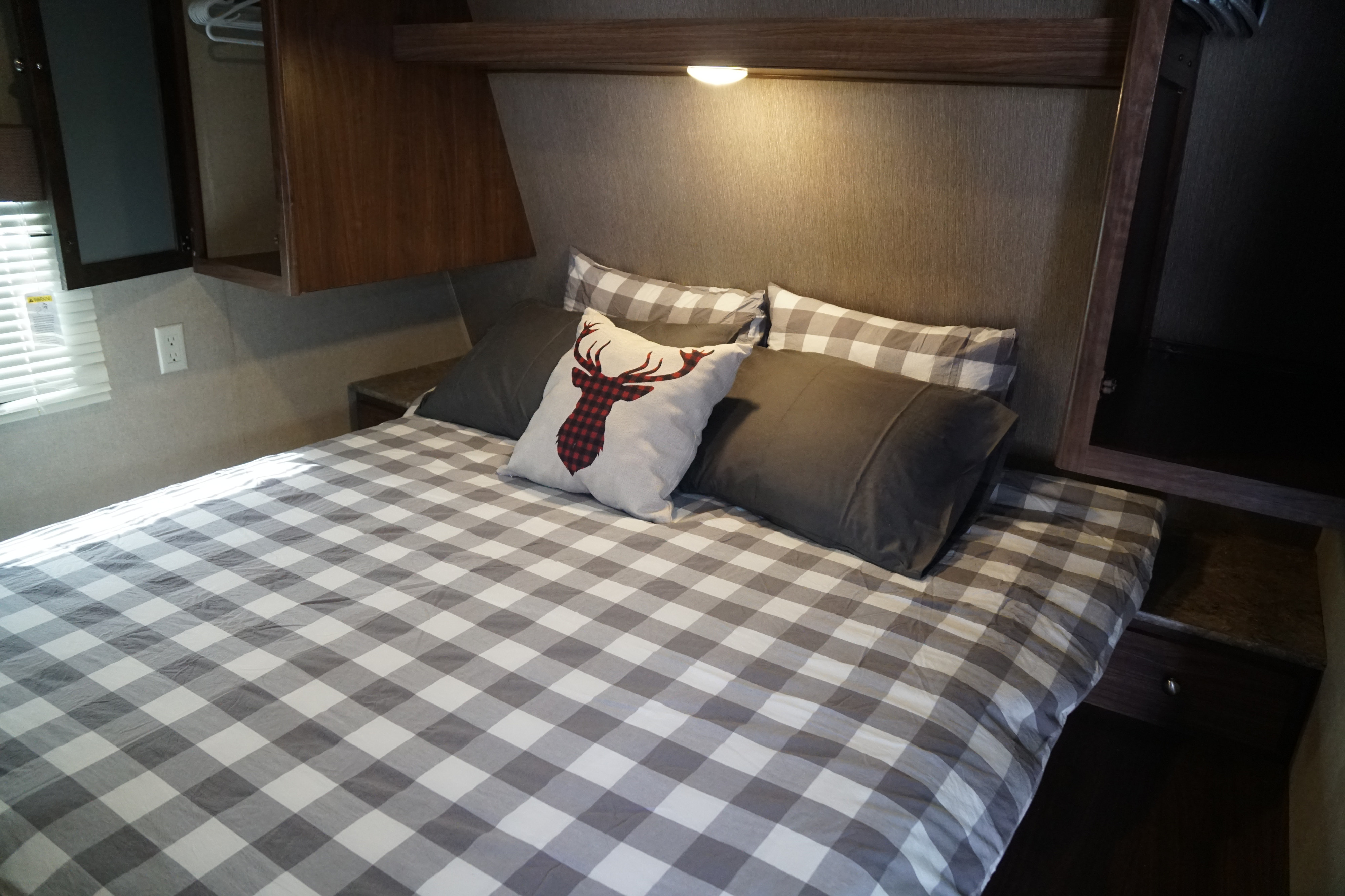 RV rental bedroom featuring a cozy bed with gray buffalo plaid bedding, a deer accent pillow, and overhead storage.. Coleman Lantern Edition 262 BH 2017