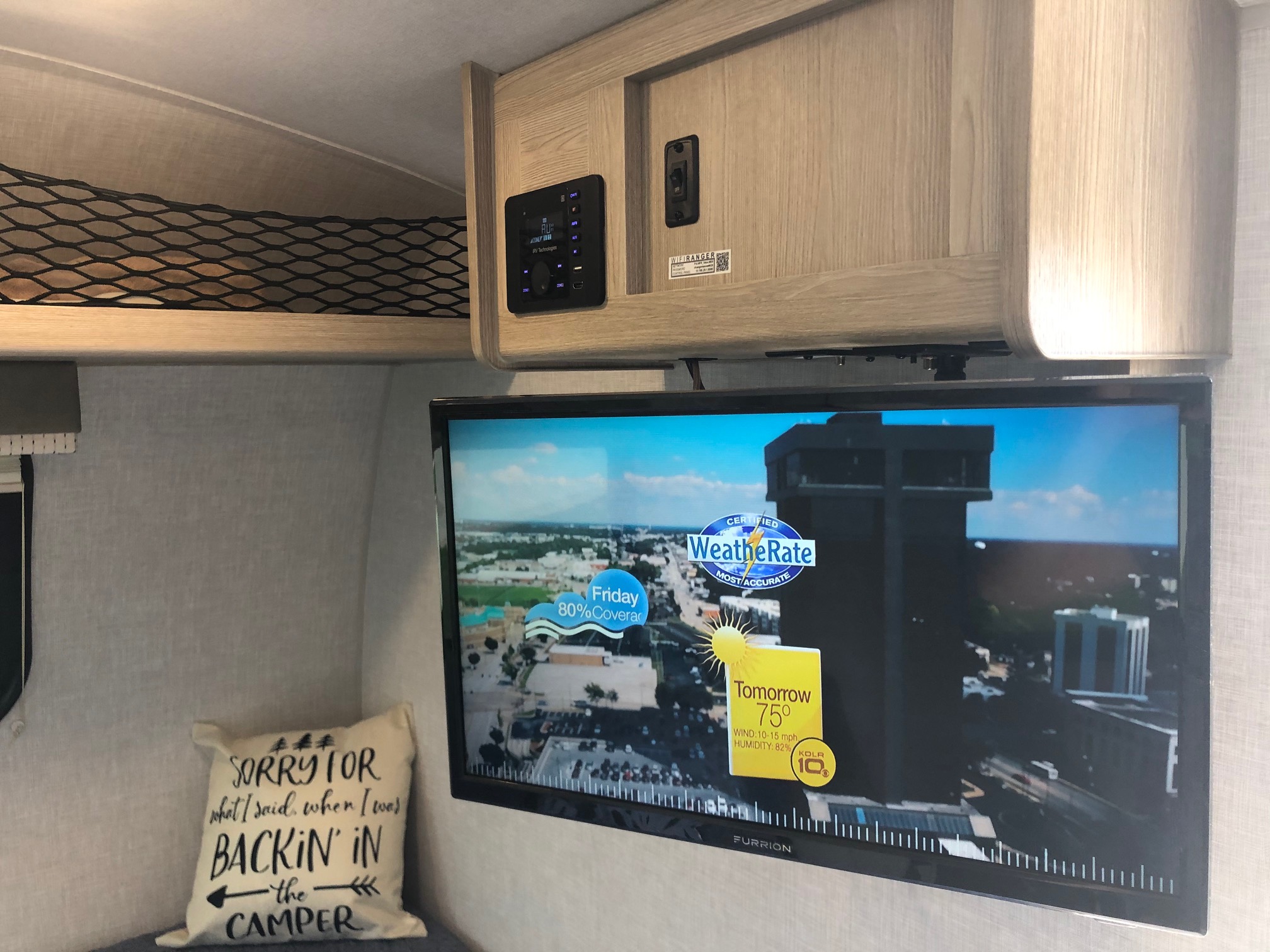 An RV rental's cozy interior features a Furrion TV displaying weather, an RV tech control panel, and net storage.. Forest River Rockwood Geo Pro 2021