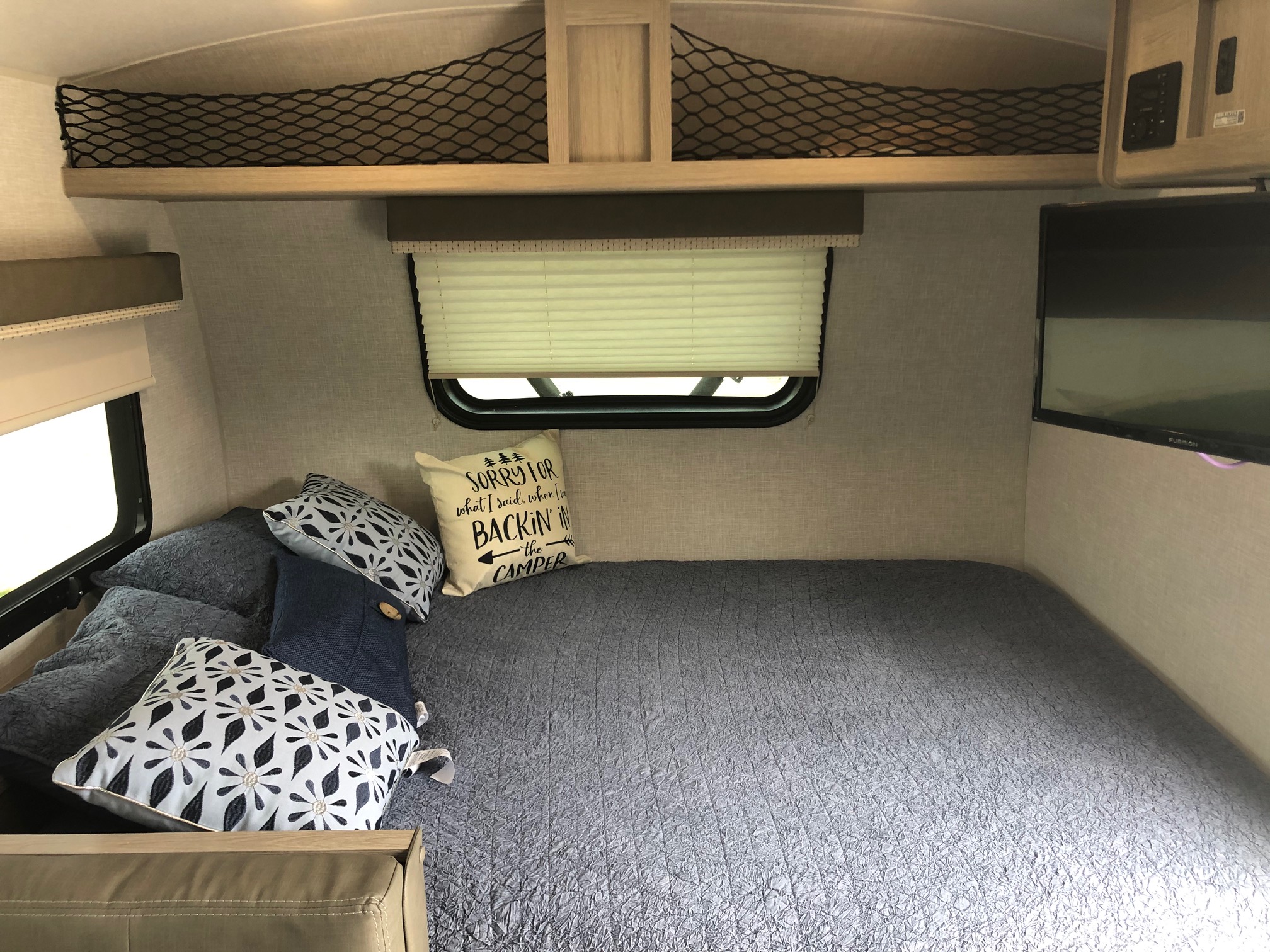 Cozy RV rental interior with a comfy bed, window, TV, and overhead net storage. Ideal for road trips!. Forest River Rockwood Geo Pro 2021