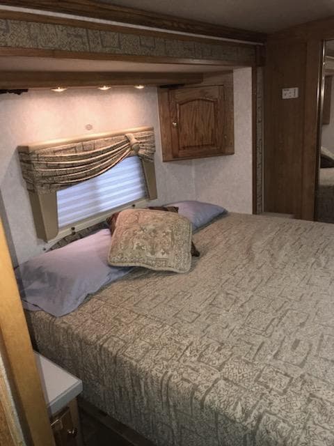 Experience comfort in this RV rental bedroom. Features a comfy bed, window with valance, overhead lighting, and wood storage.. Tiffin Motorhomes Allegro Bay 2001