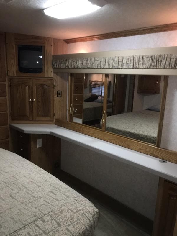 RV rental interior showing a bedroom with bed, wood cabinetry, TV, and mirrored vanity.. Tiffin Motorhomes Allegro Bay 2001
