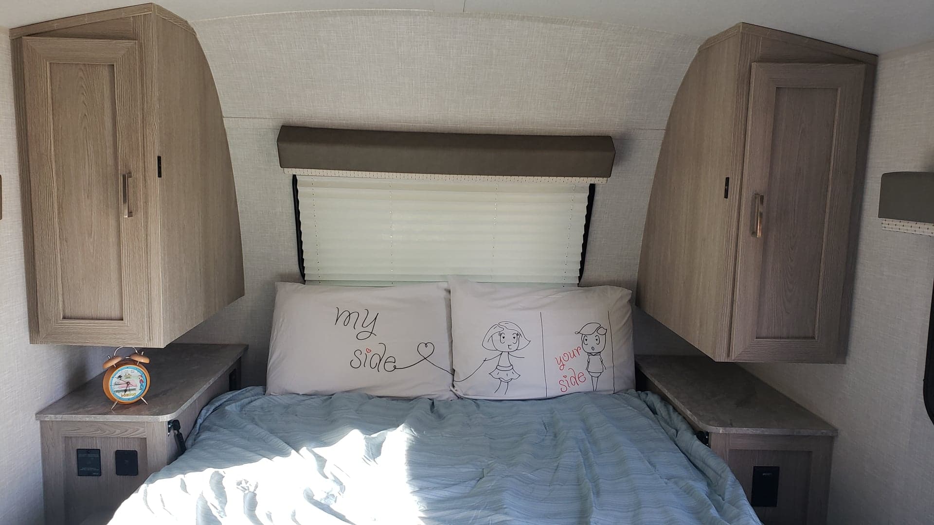 Inside an rv rental, this cozy RV bedroom features a bed with 'my side' & 'your side' pillows, cabinets & window.. Forest River Rockwood 2021