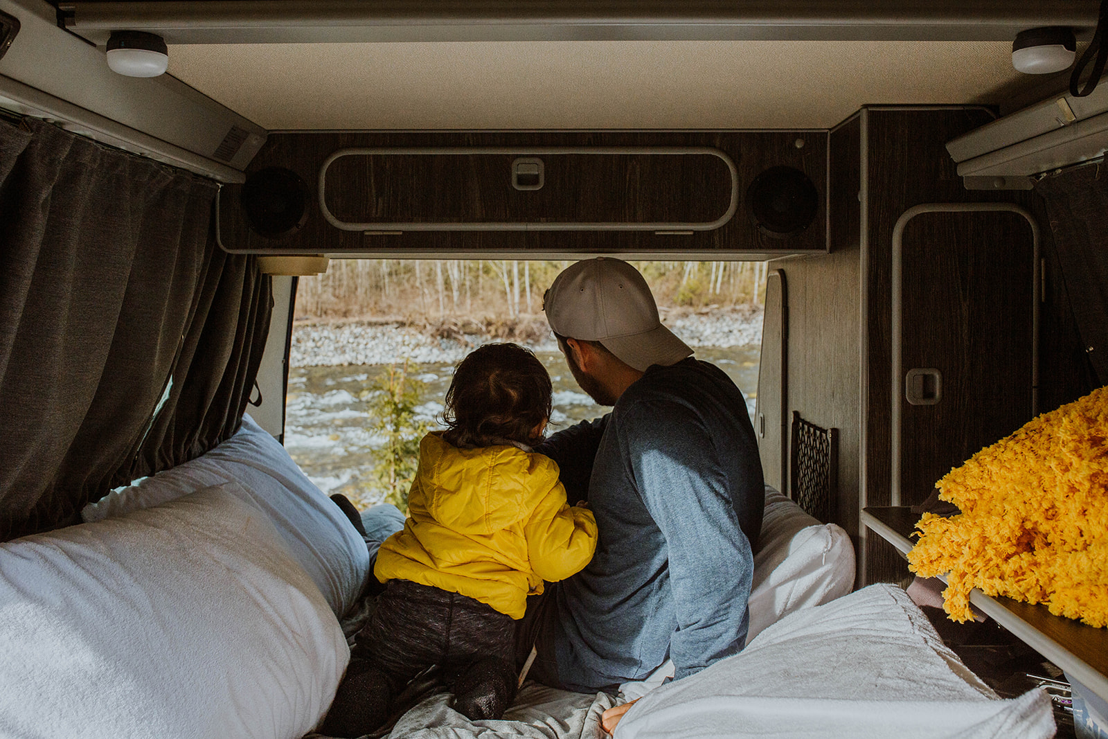 Inside an **RV rental**: Father and child gaze at a scenic river view from their comfortable camper bed, enjoying family travel.. Volkswagen Vanagon 1990