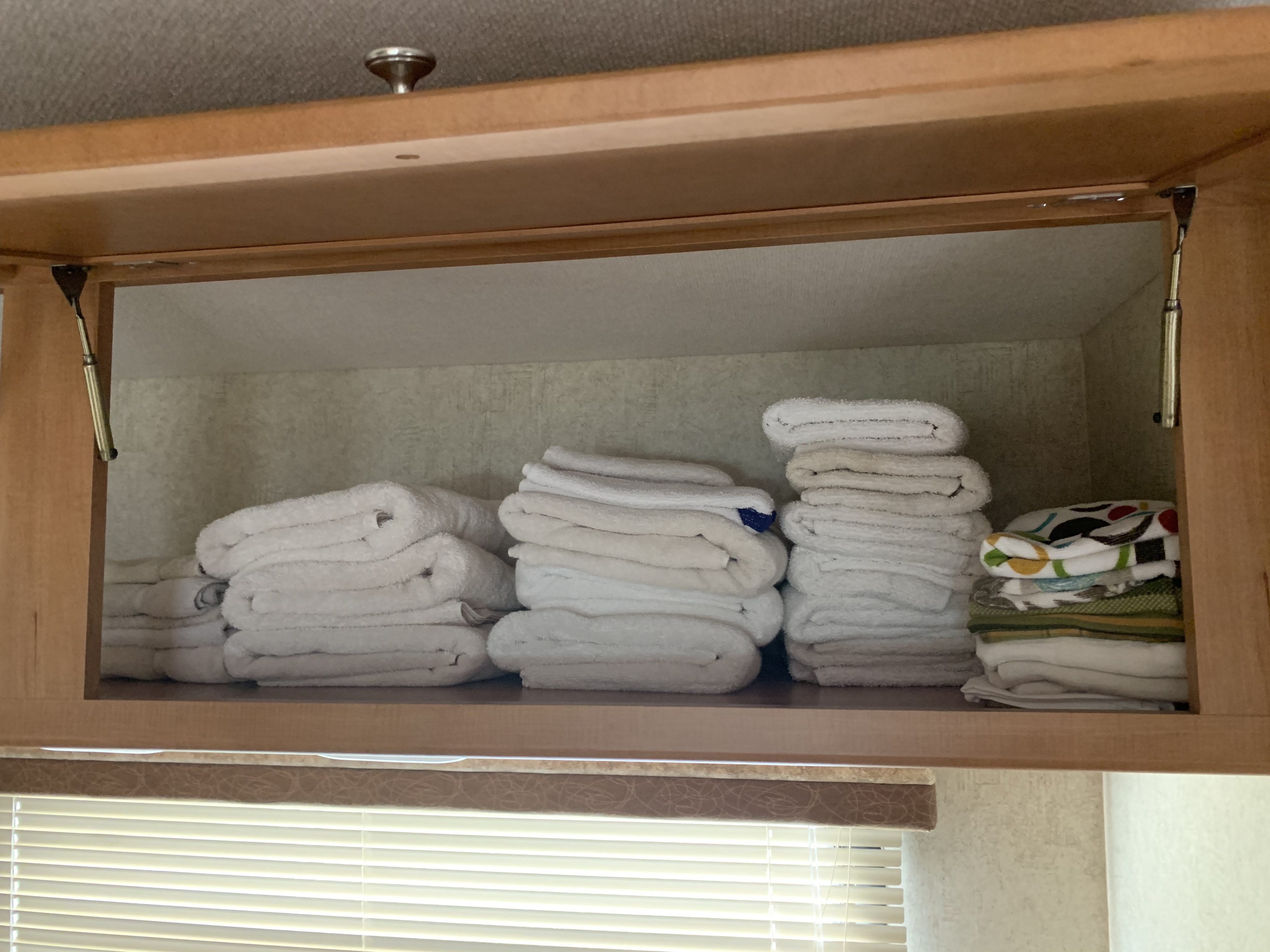 Organized overhead storage in an RV rental: neatly folded white and colorful towels and linens are stacked inside.. Winnebago Access 2007