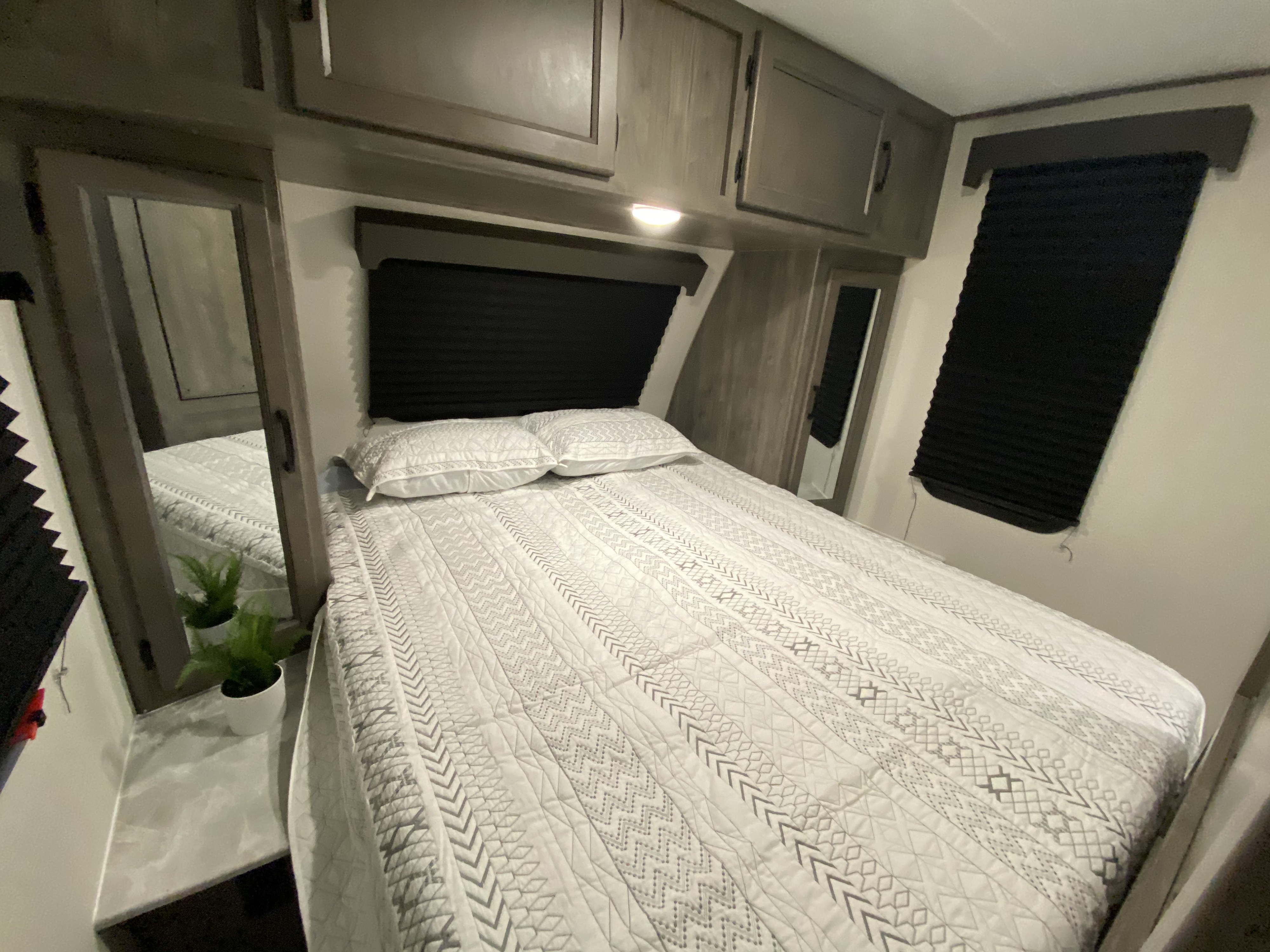 Spacious RV rental bedroom with patterned bedding, overhead cabinets, mirrors, and privacy blinds, perfect for your next trip.. Coachmen Apex 2021
