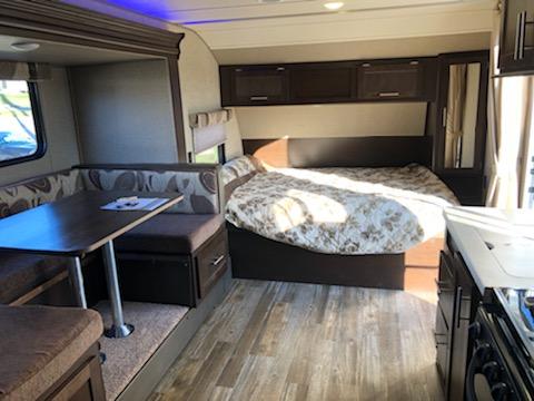 Interior of an RV rental showing a bed, dinette with table, and partial kitchen. Ideal for travel comfort.. Forest River Cherokee Grey Wolf 2017