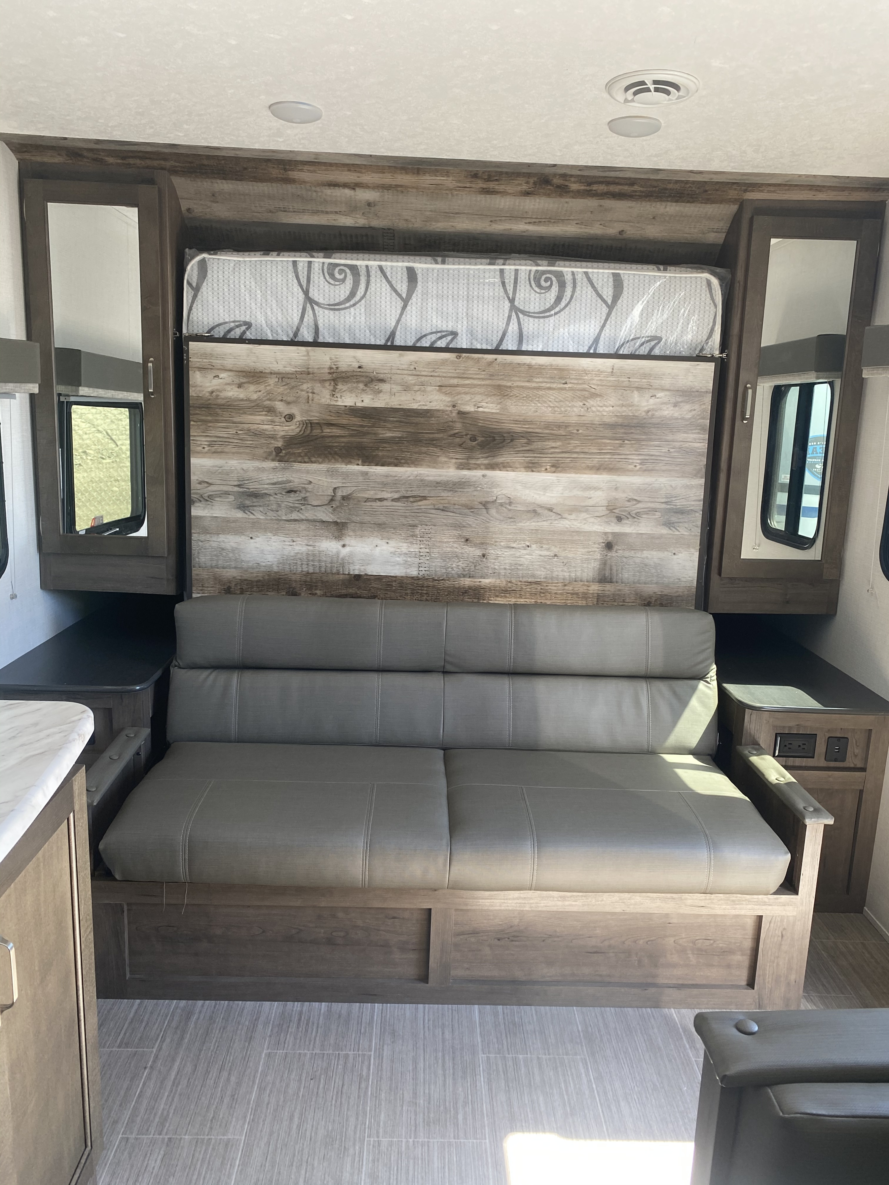 RV rental interior: Versatile living space with a gray sofa that converts to a murphy bed, surrounded by wood-paneled storage.. Keystone Passport 2021