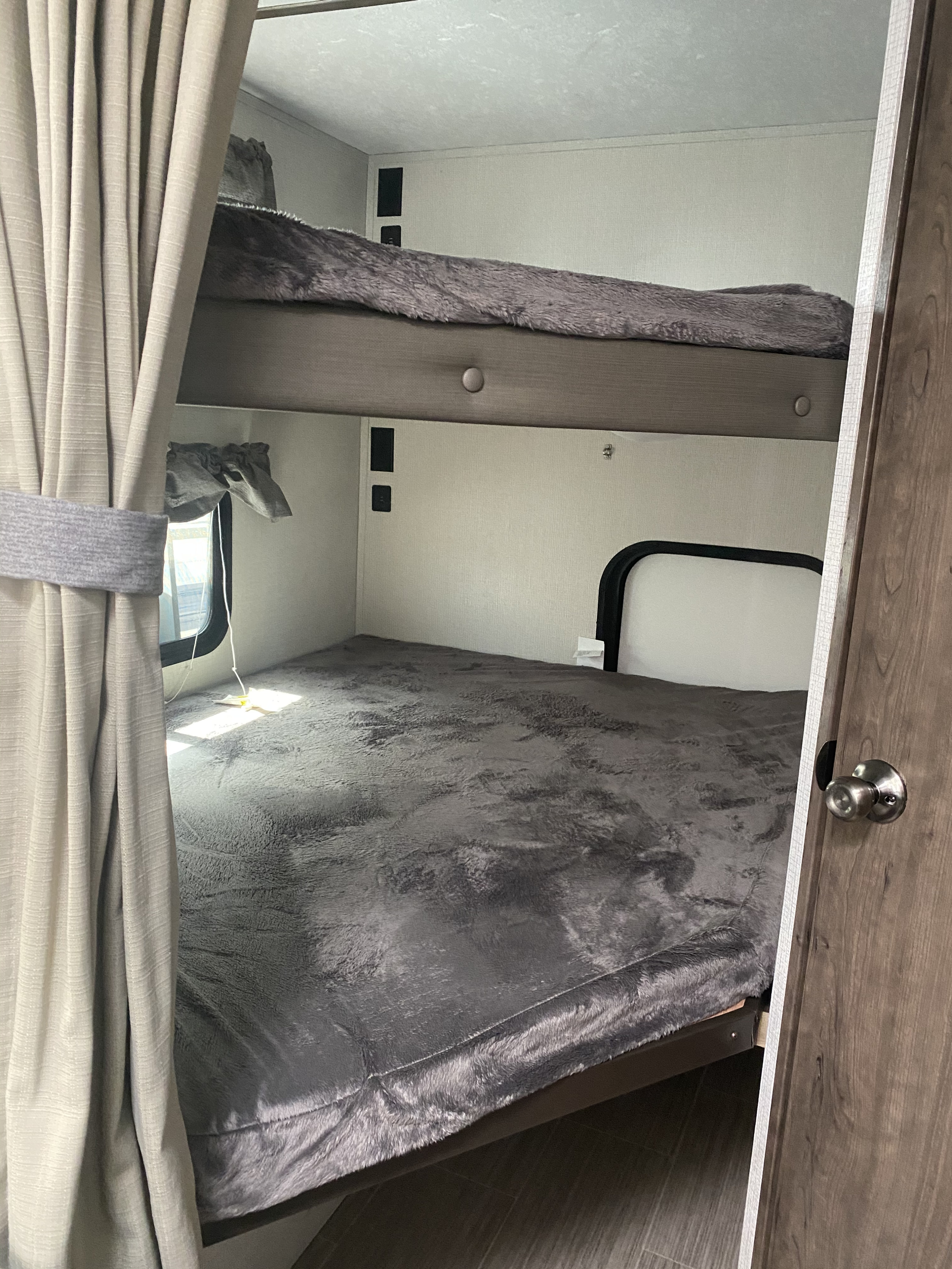 Cozy bunk beds inside an RV rental, featuring soft grey blankets, privacy curtain, and a comfortable sleeping area.. Keystone Passport 2021