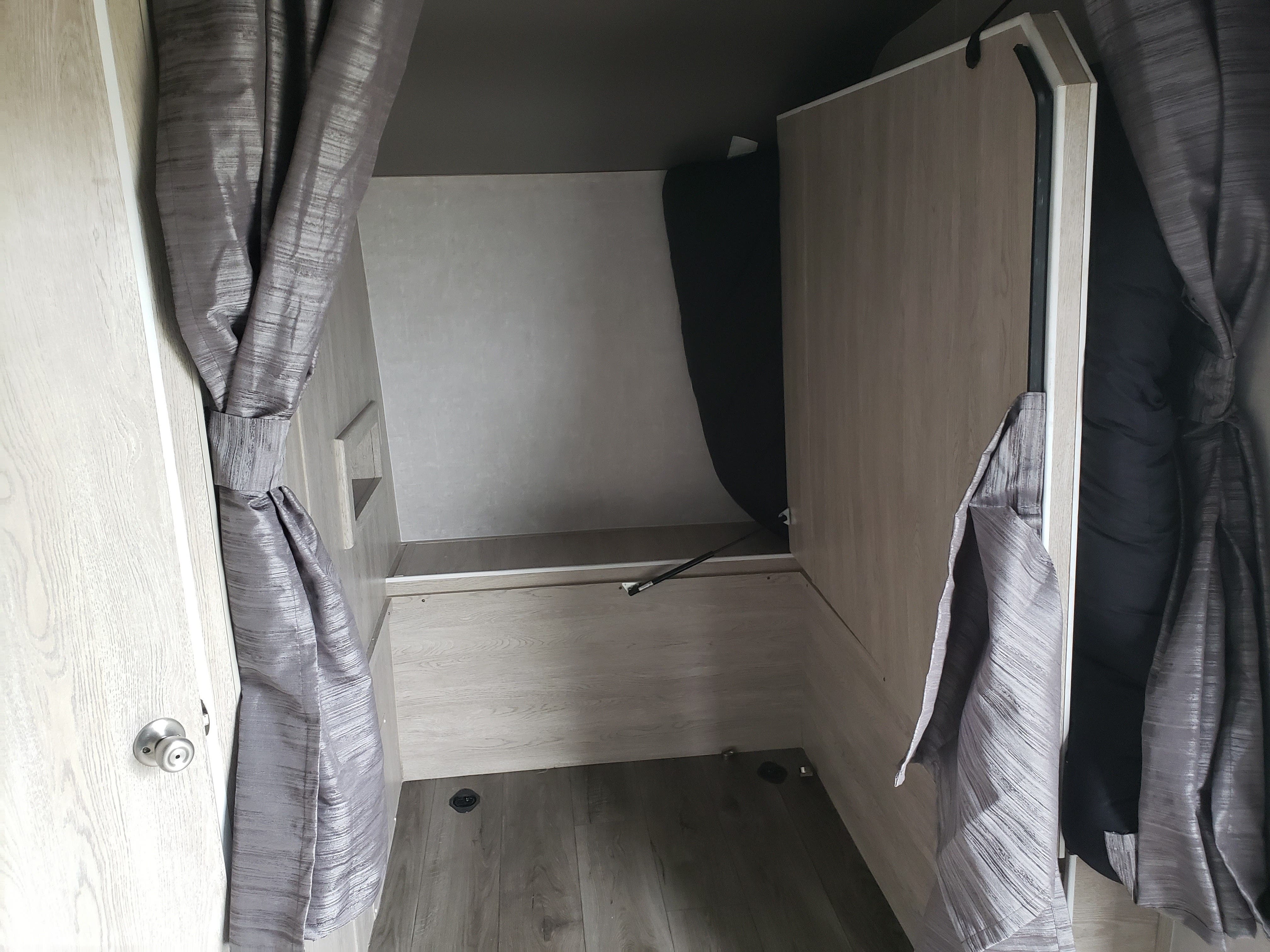 Compact RV rental interior: A light wood-paneled sleeping area with grey tie-back curtains. Includes a bed platform and floor.. Eclipse Recreational Vehicles Attitude 2020
