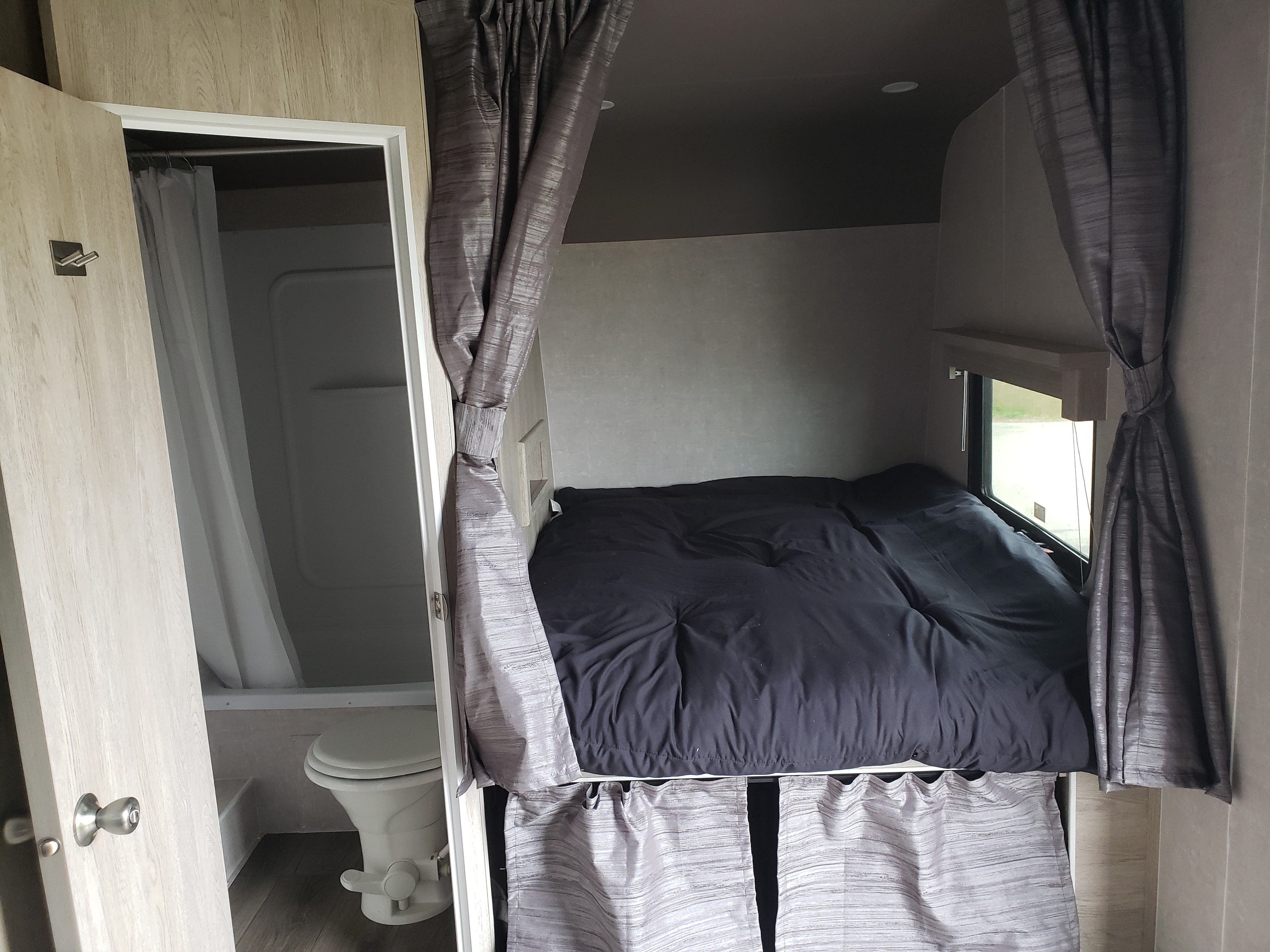 RV rental interior shows compact bedroom with black bedding, window, and adjacent bathroom with toilet.. Eclipse Recreational Vehicles Attitude 2020