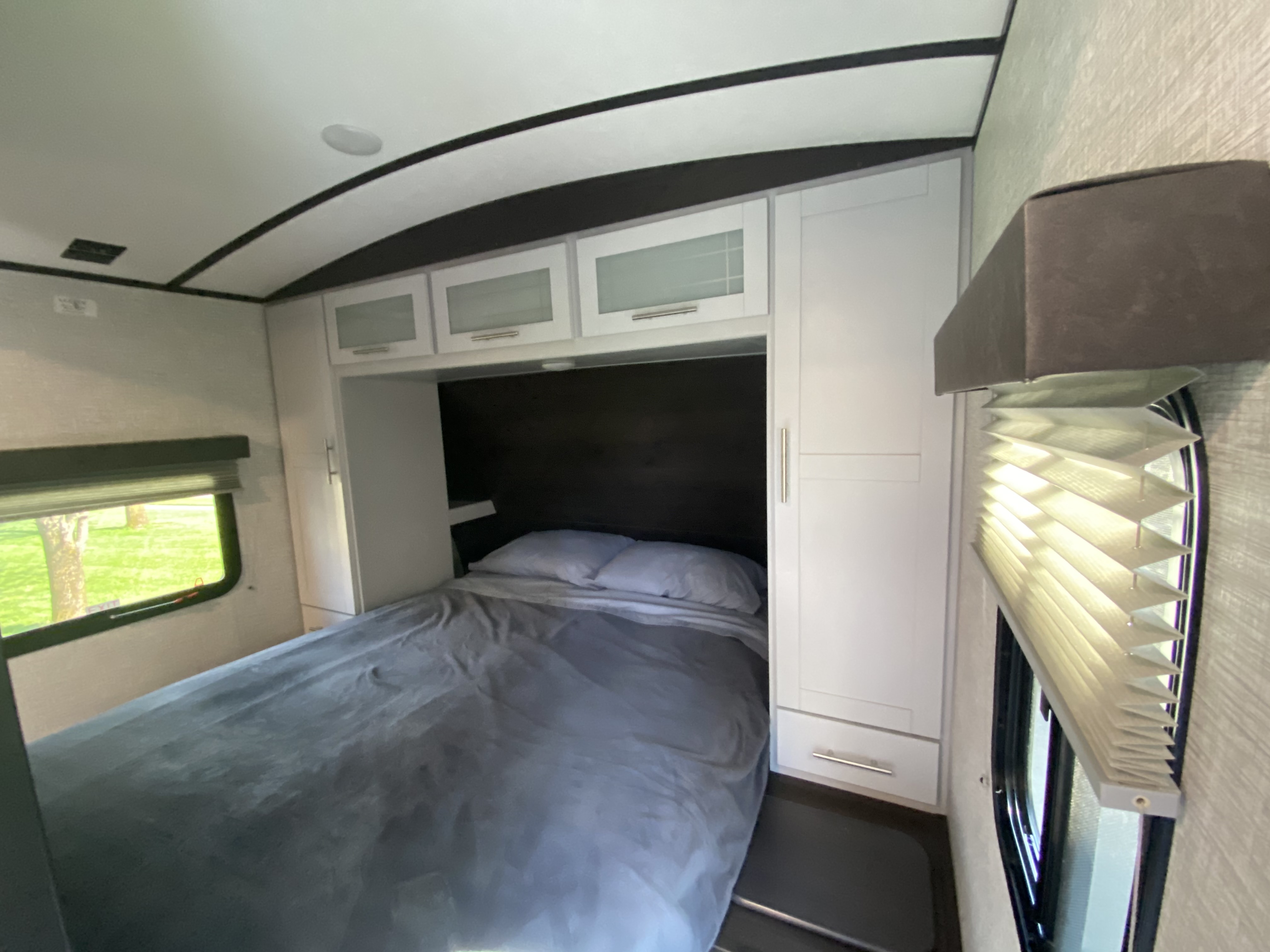 RV rental bedroom interior with a comfortable bed, white storage cabinets, and large windows with outdoor views.. Keystone RV Bullet Ultra Lite 2021