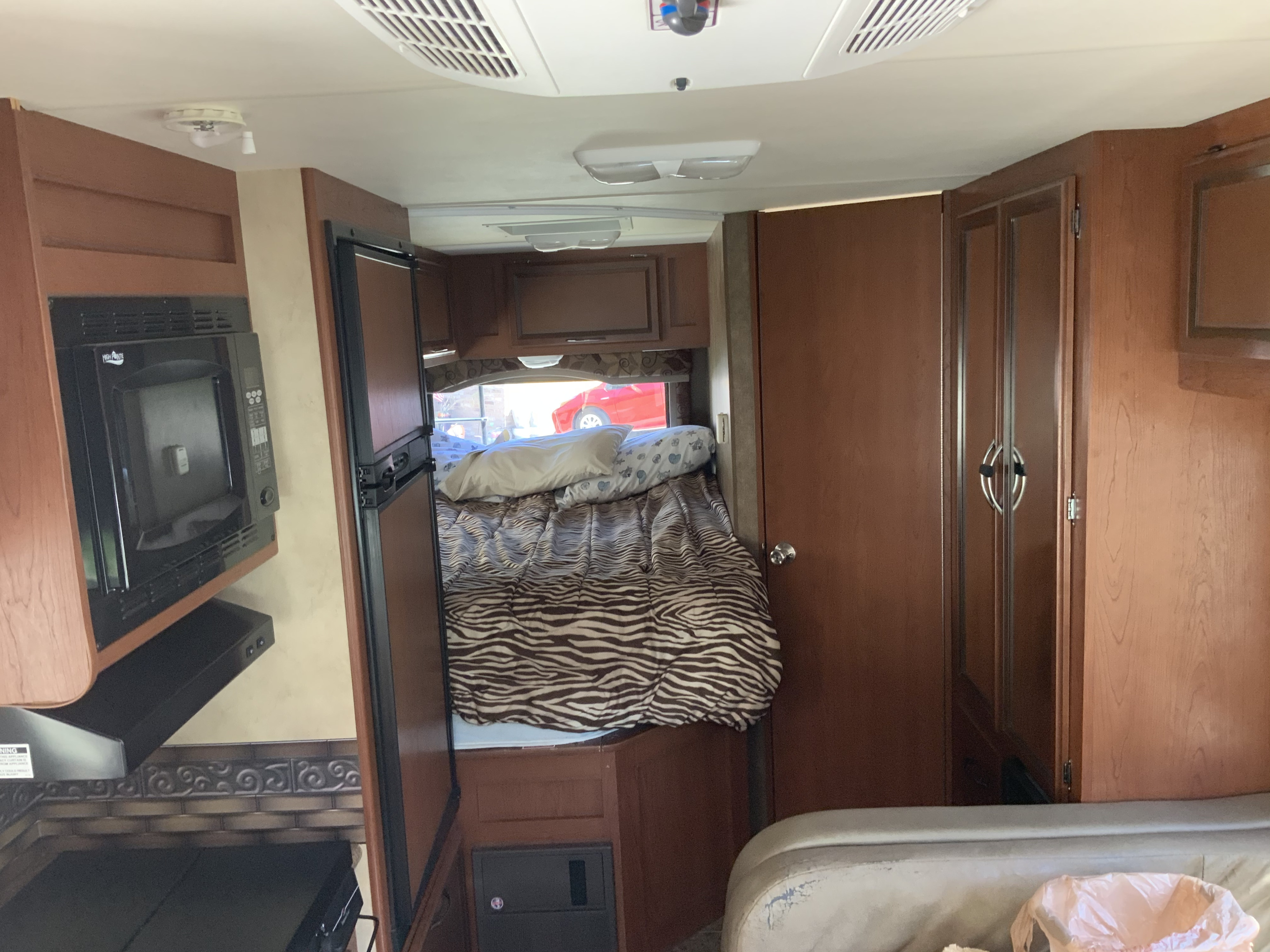 RV rental interior: cozy bed with zebra comforter, kitchen with microwave & fridge, and sofa seating.. Thor Motor Coach Four Winds 2013