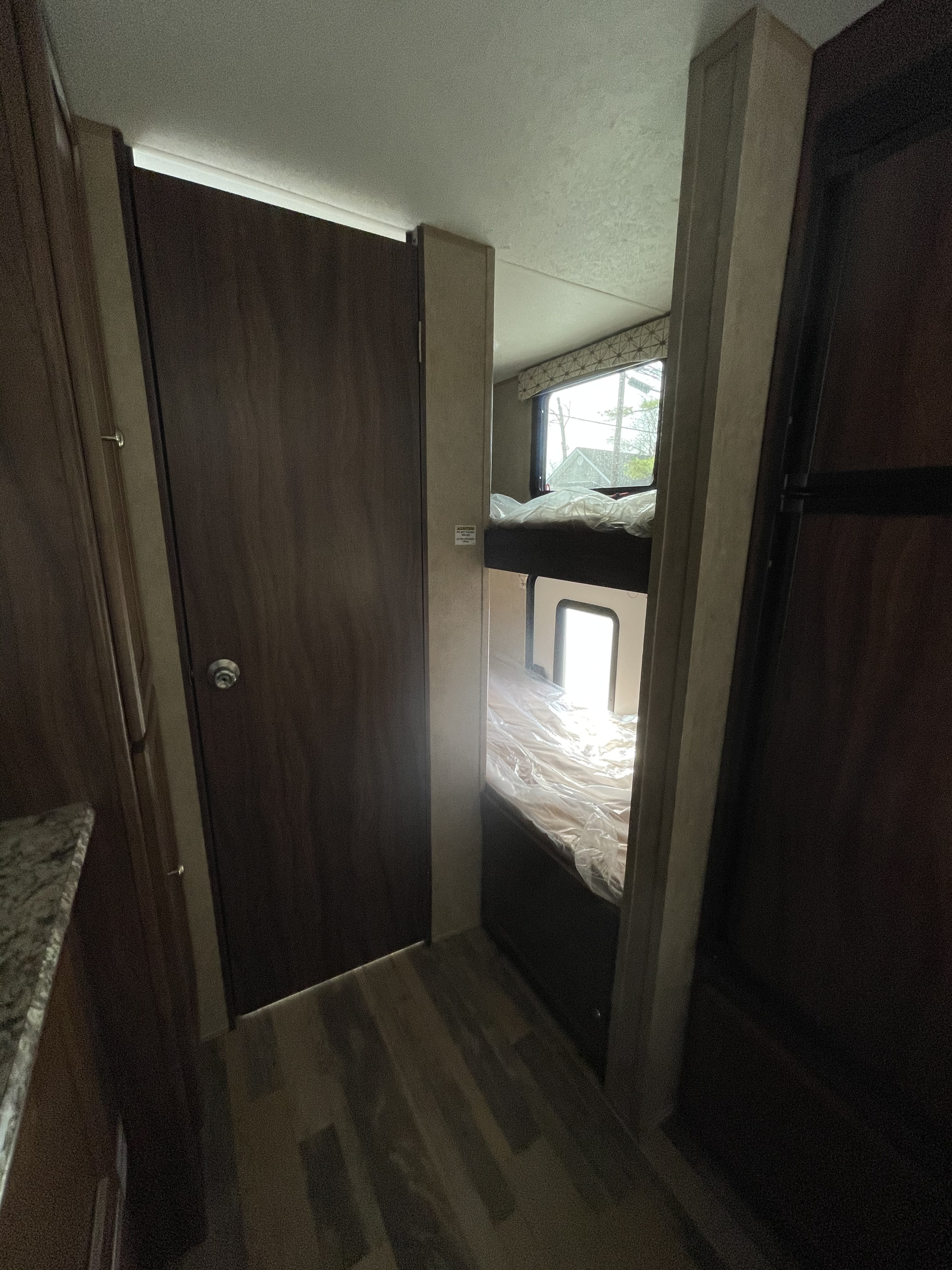 Inside this RV rental, a narrow hallway with a closed door leads to bunk beds, featuring plastic-covered mattresses and a window.. Viking 21BH 2018
