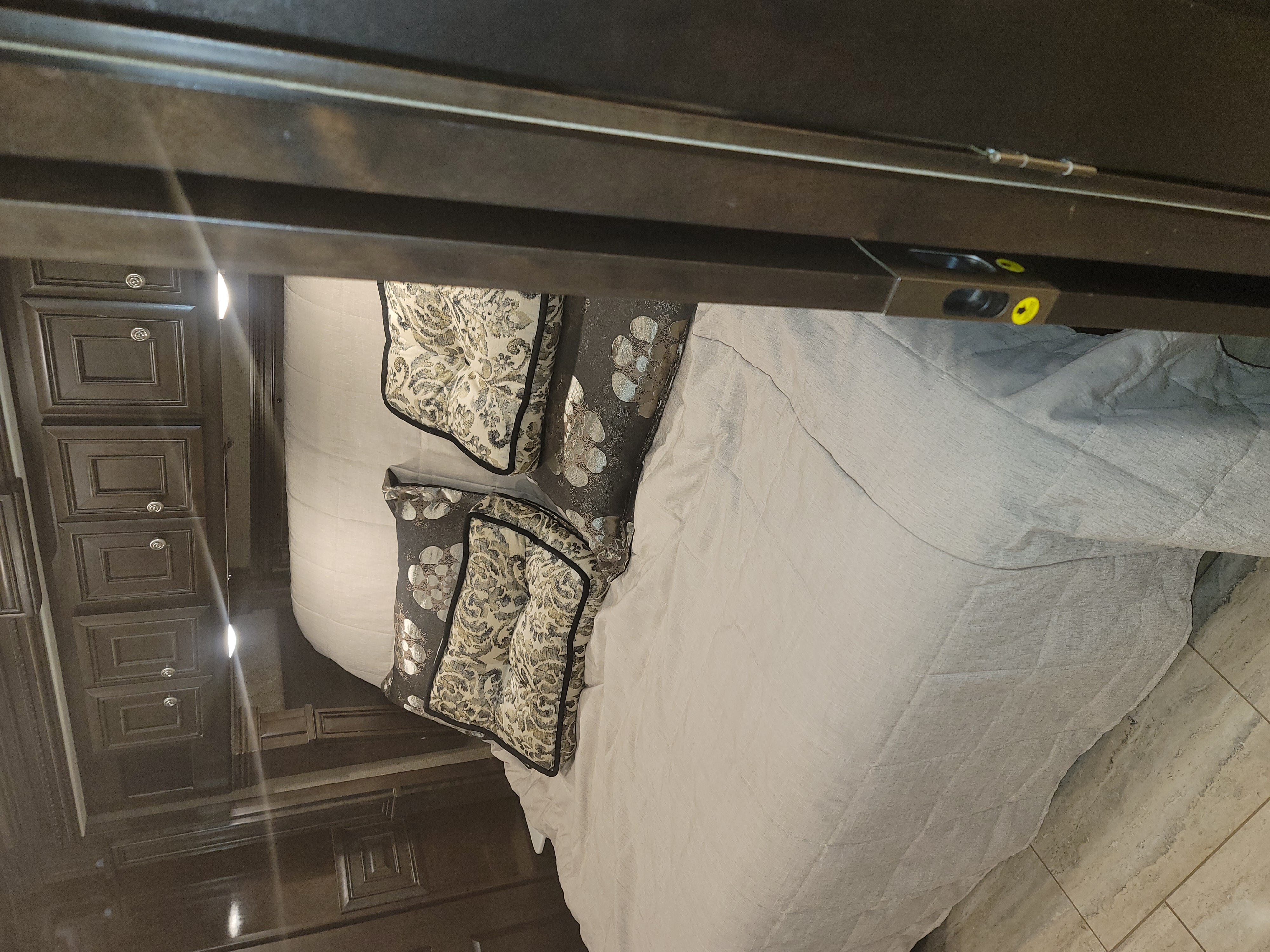 Cozy RV rental bedroom featuring a bed with patterned pillows, light-colored bedding, rich wood cabinets, and built-in lights.. Monaco Marquis 2019