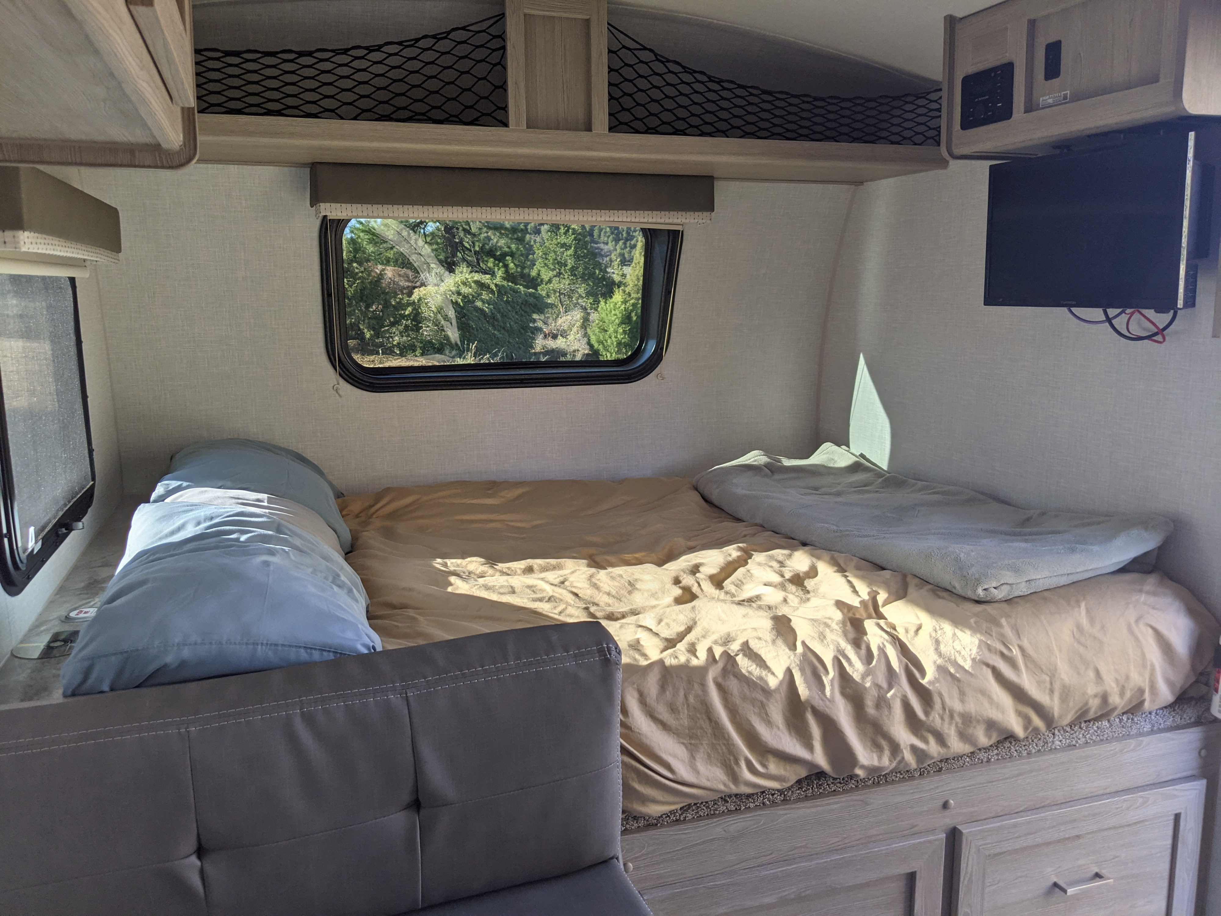 Cozy RV rental interior with a bed, window view of trees, and a mounted TV, perfect for travel.. Forest River Geo Pro 19BH 2021