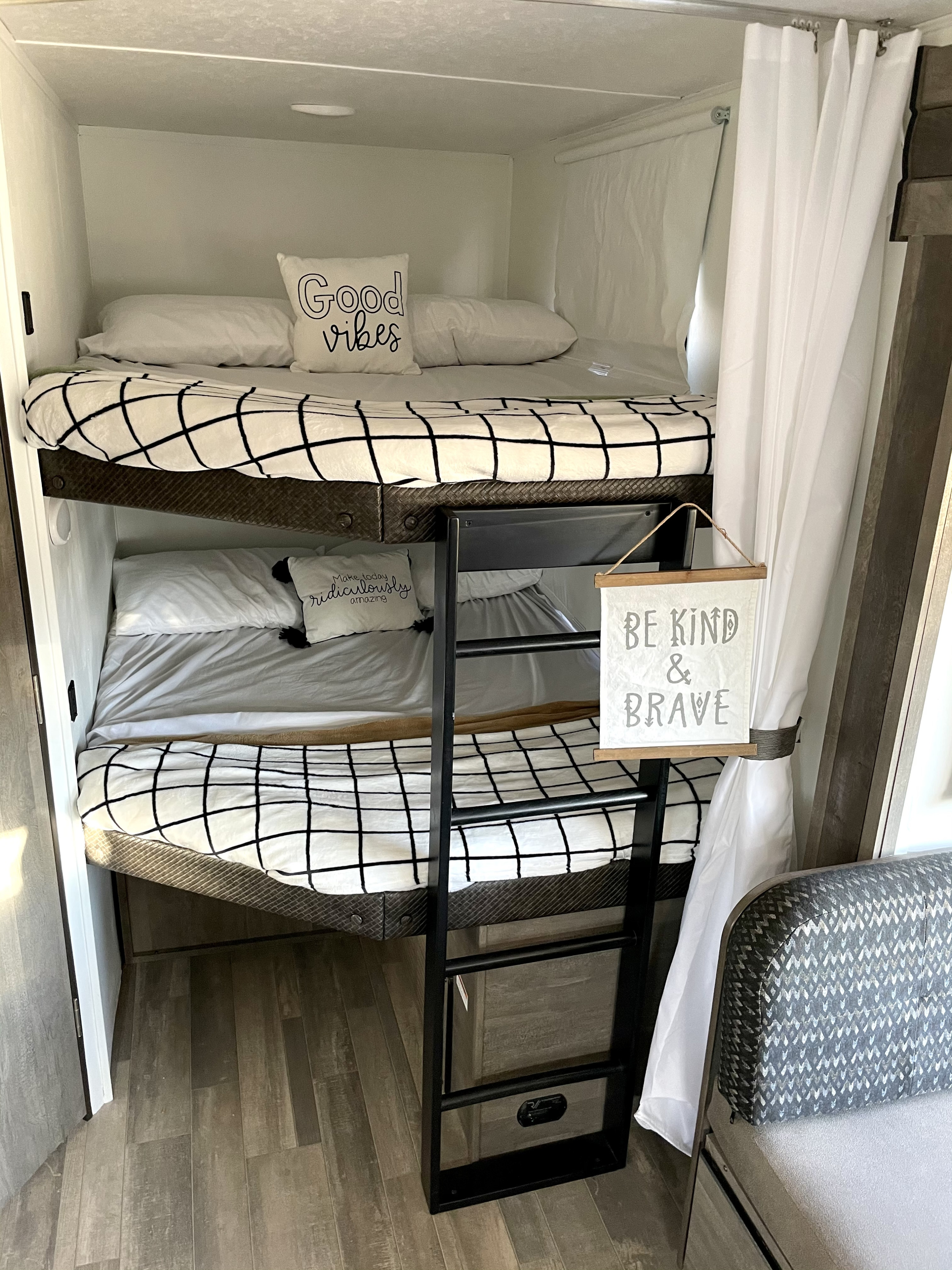 Step inside this RV rental's cozy bunk bed area, featuring checkered bedding & inspirational signs for a comfy stay.. Forest River Vibe 2021