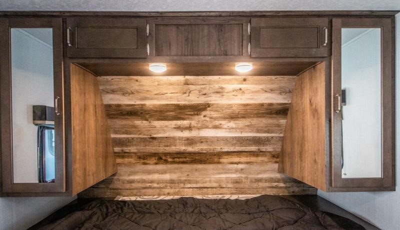 RV rental bedroom: Rustic plank headboard with functional overhead storage, mirrored cabinets, and task lighting.. Keystone Passport 2021