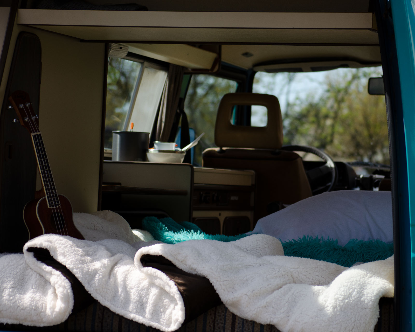 Cozy RV rental interior with bed, ukulele, and mini kitchen setup for travel.. Volkswagen Vanagon 1984