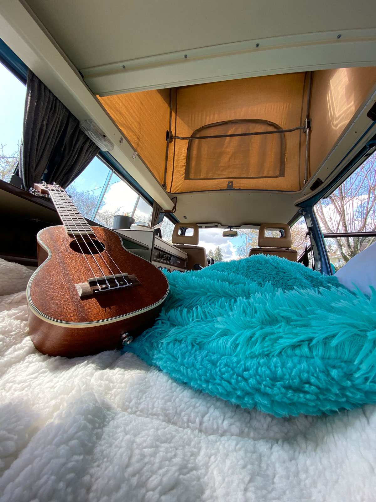 Inside a cozy RV rental camper: ukulele on fluffy bedding with a pop-top open for views.. Volkswagen Vanagon 1984