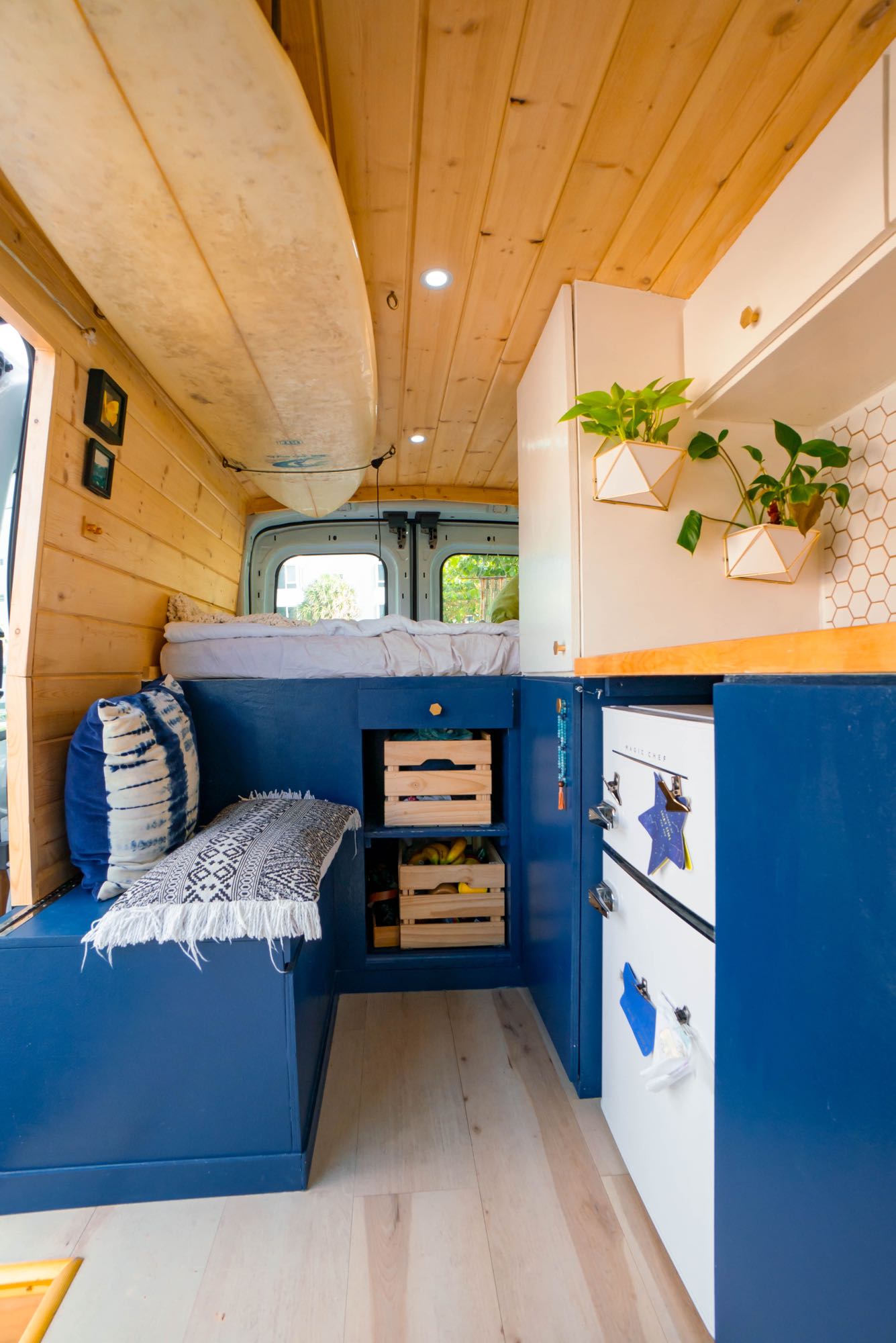 Cozy RV rental interior with wooden walls, custom blue cabinetry, a mounted surfboard, and plants.. Ford Transit Custom 2020