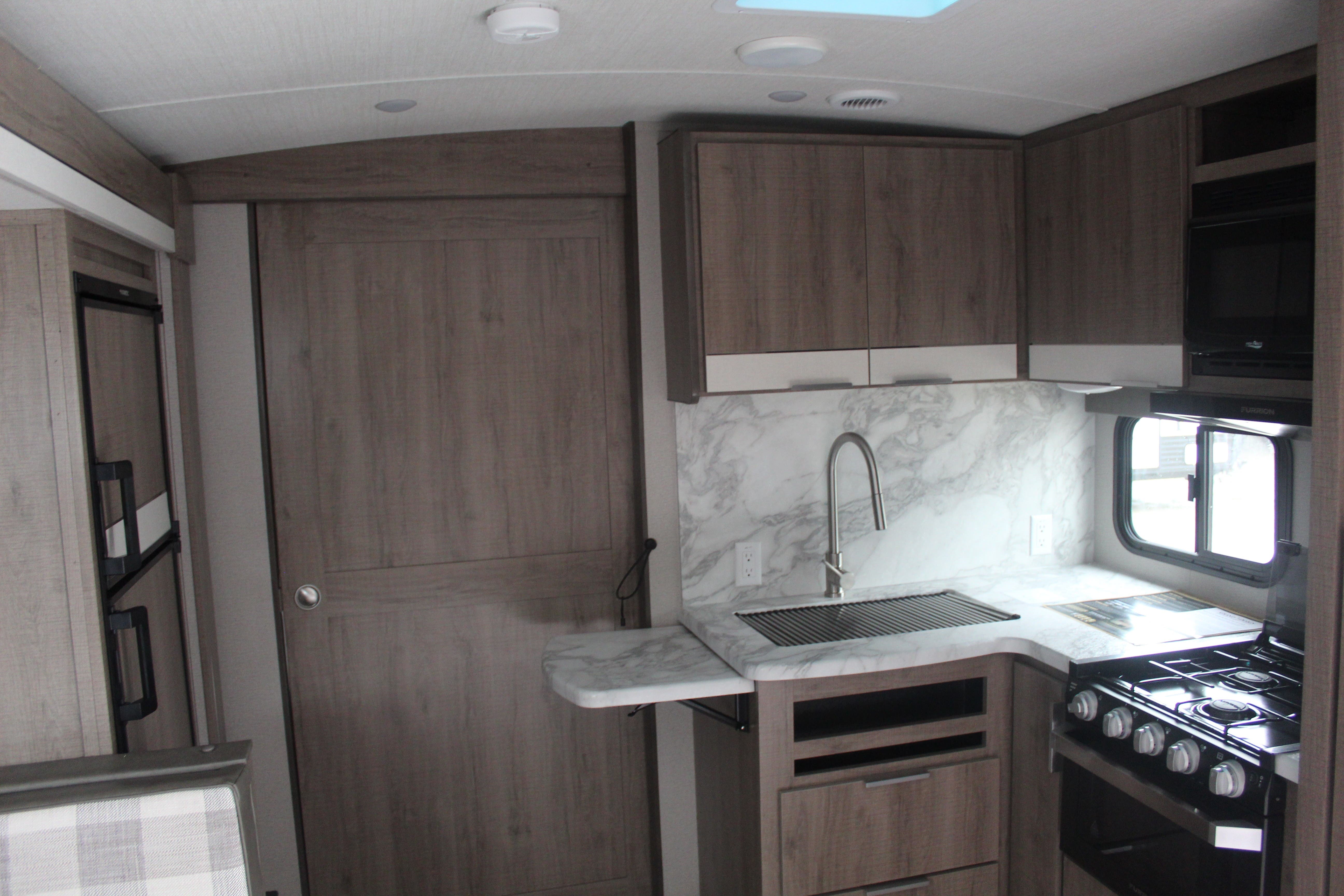 Compact RV rental interior showcasing a well-equipped kitchen with a sink, stove, microwave, and wood-toned cabinets.. Grand Design 2400BH 2022