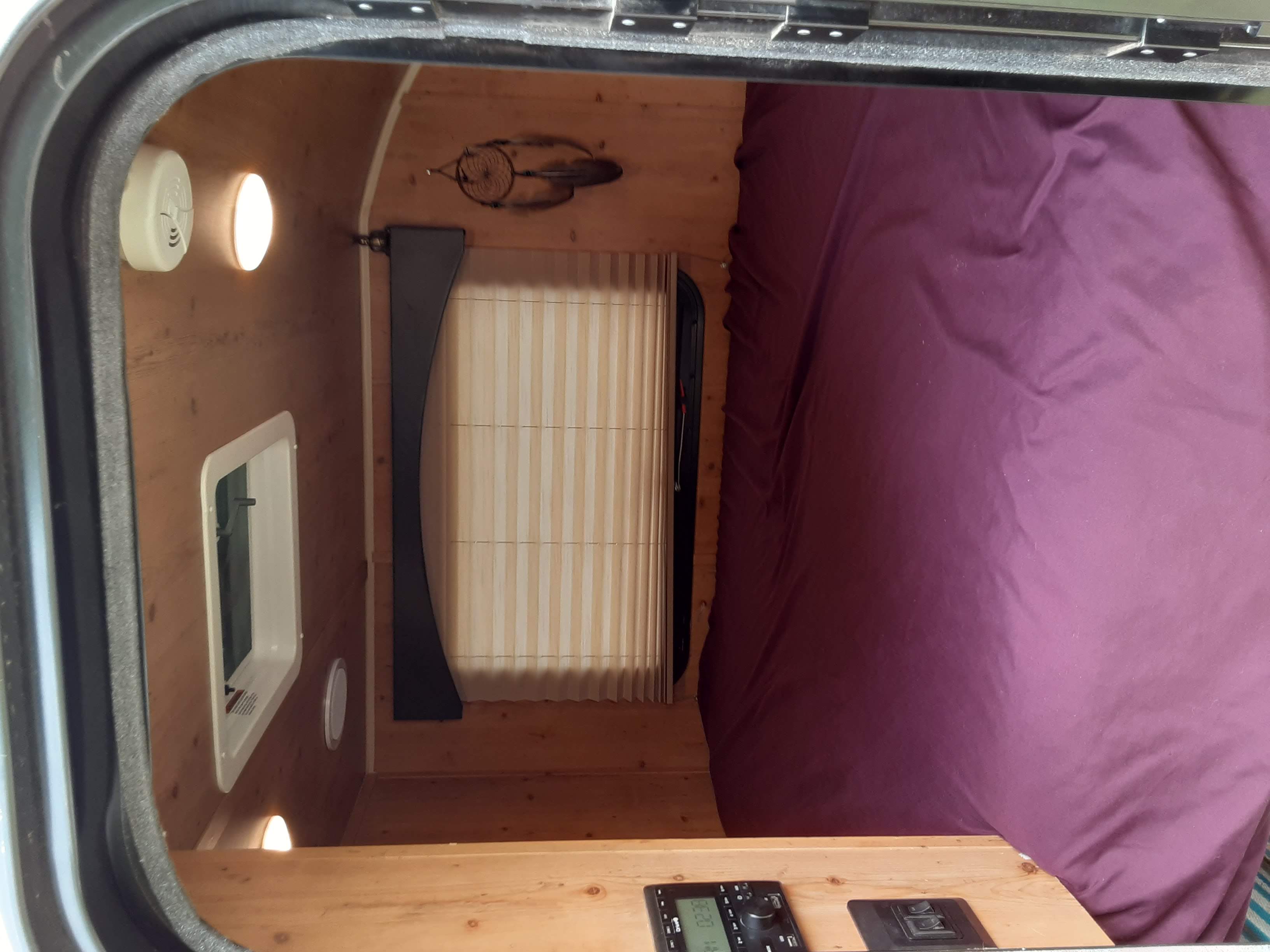 Cozy RV rental interior: a wood-paneled bedroom with purple bedding, windows, and a control panel for comfortable travel.. Sunset Park & Rv Inc. 14' 2020