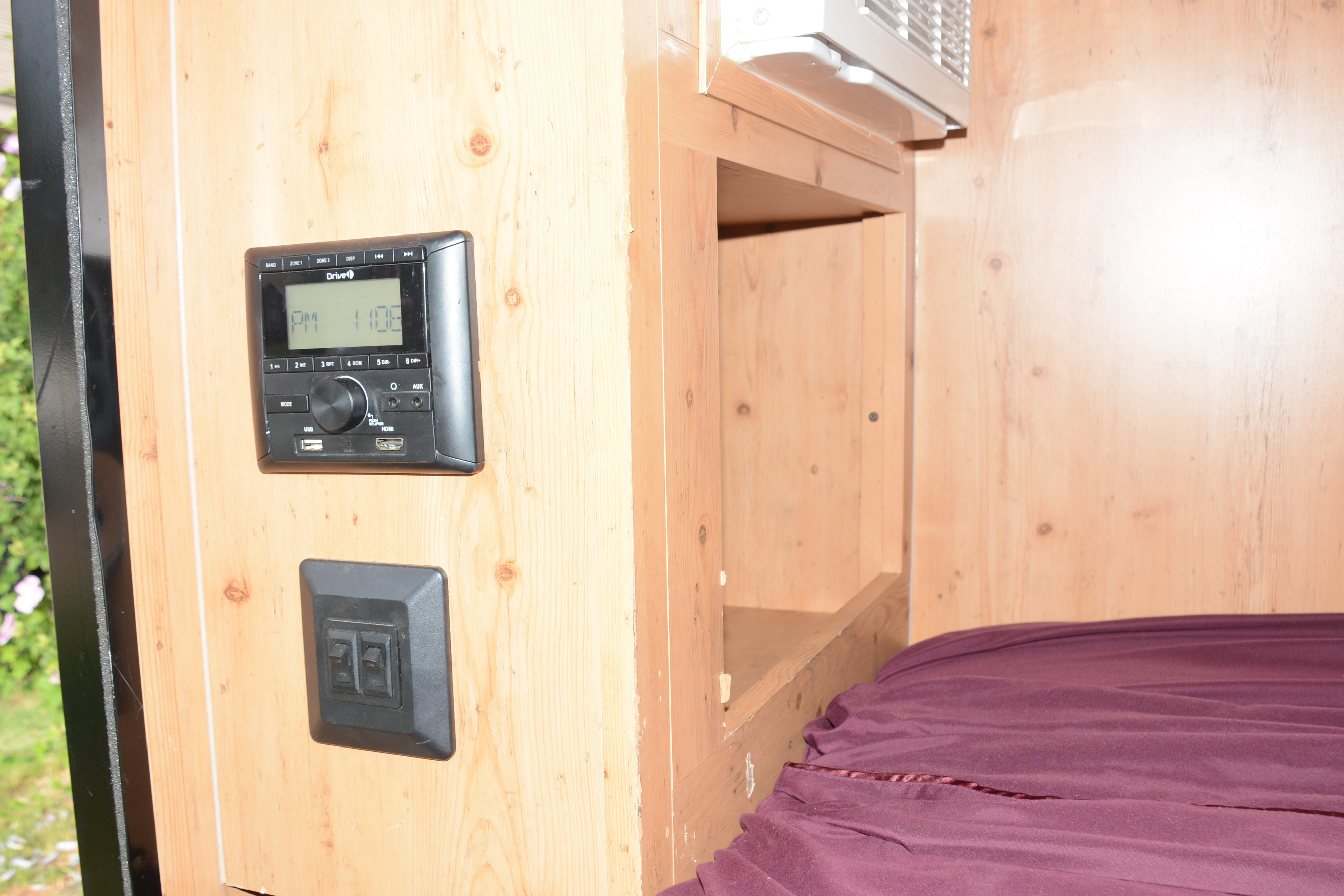 This RV rental interior features a mounted stereo, light switches, AC unit, bed, and wooden walls.. Sunset Park & Rv Inc. 14' 2020