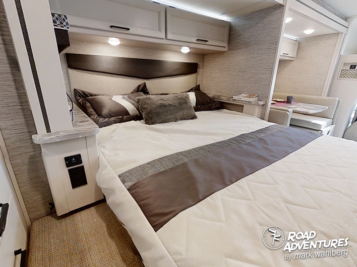 Cozy RV rental bedroom featuring a comfortable bed with neutral linens, overhead storage, and a glimpse of the dining area.. Thor Motor Coach Gemini 23TW 2022