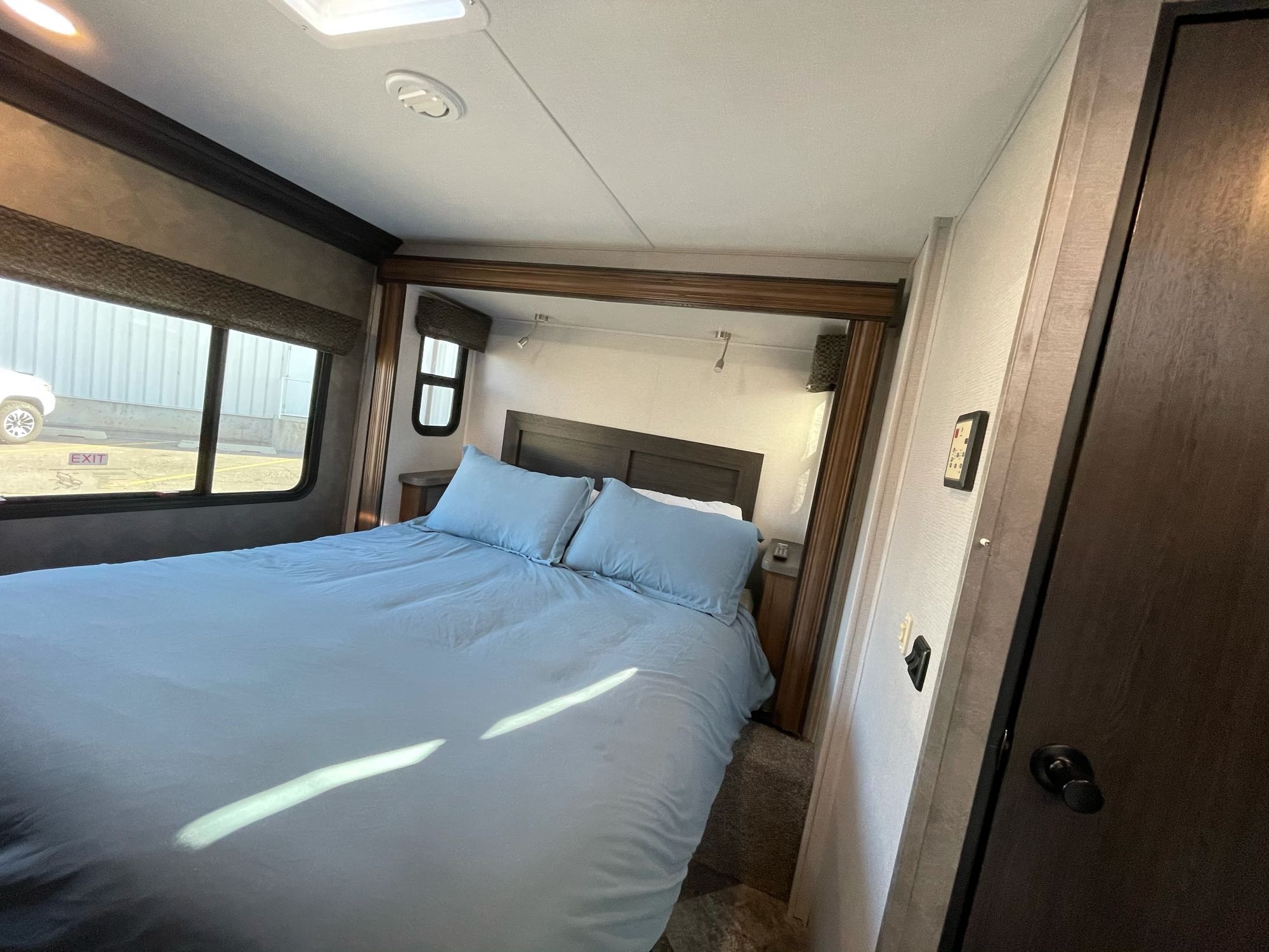 This inviting RV rental bedroom features a comfortable blue bed, windows, and overhead lights. Perfect for a cozy travel experience.. Forest River Sunseeker 2021