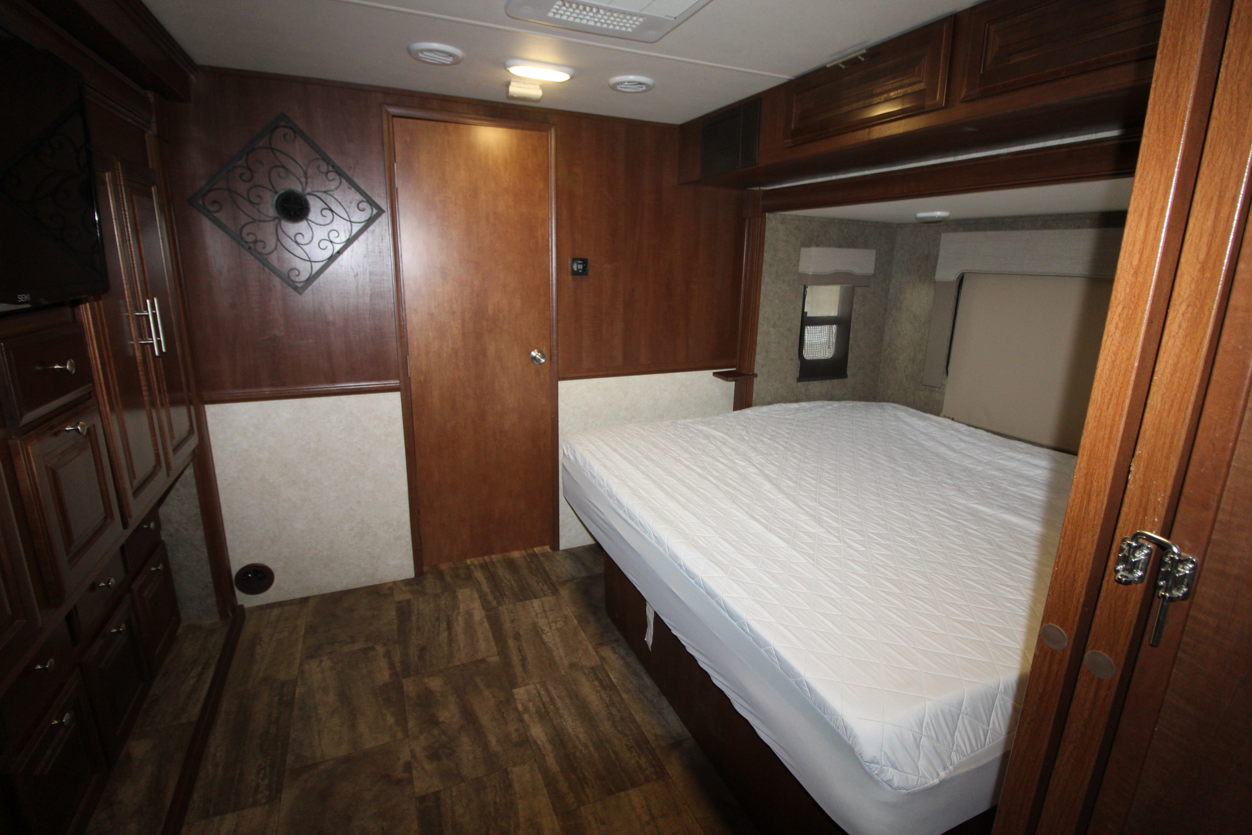 RV rental bedroom interior: comfortable bed with white mattress, warm wood paneling, cabinets, door, and laminate floor.. Forest River Georgetown 2017