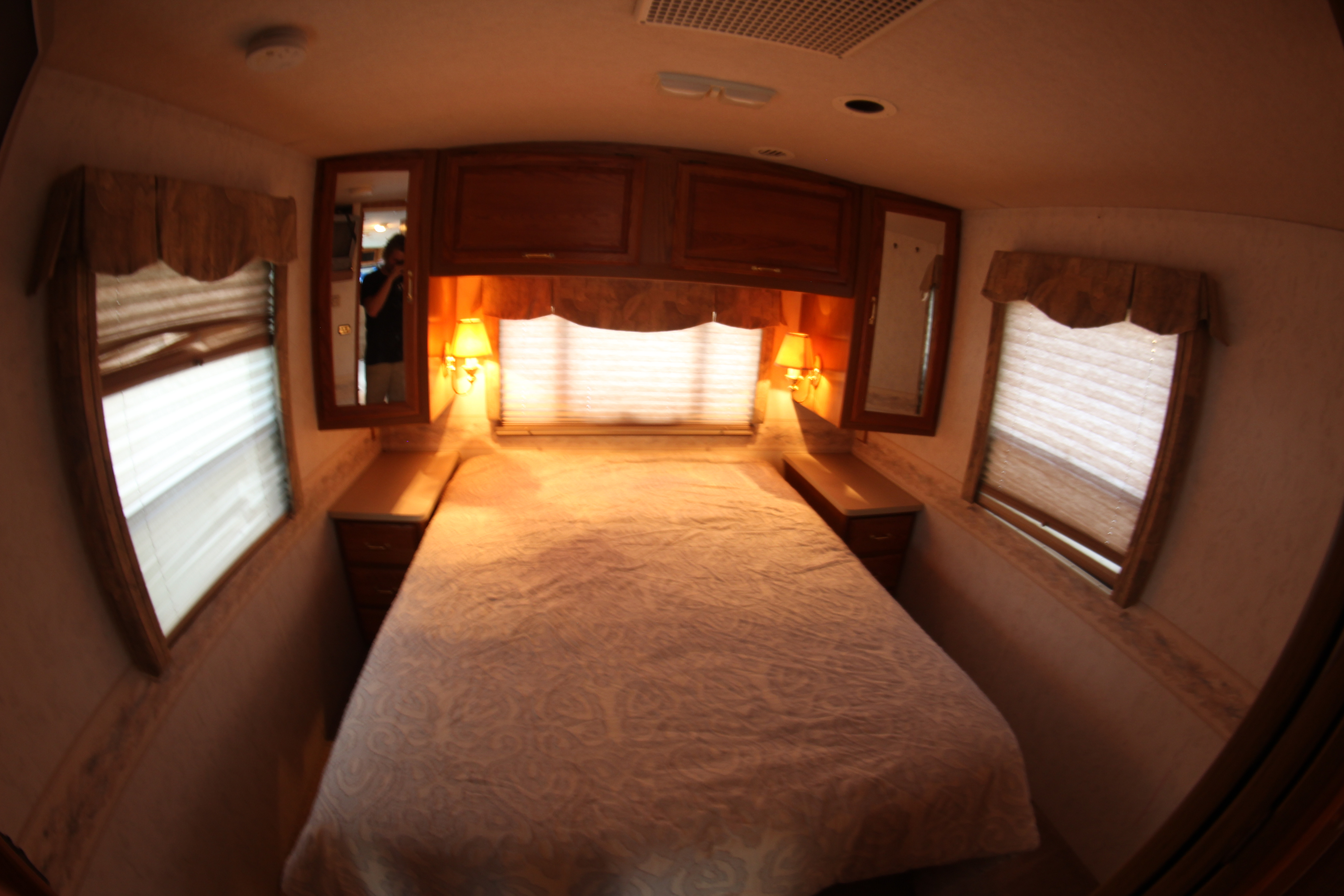 A cozy RV rental bedroom interior with a comfortable bed, wood cabinetry, and bedside lamps, perfect for your journey.. Winnebago Adventurer 1999