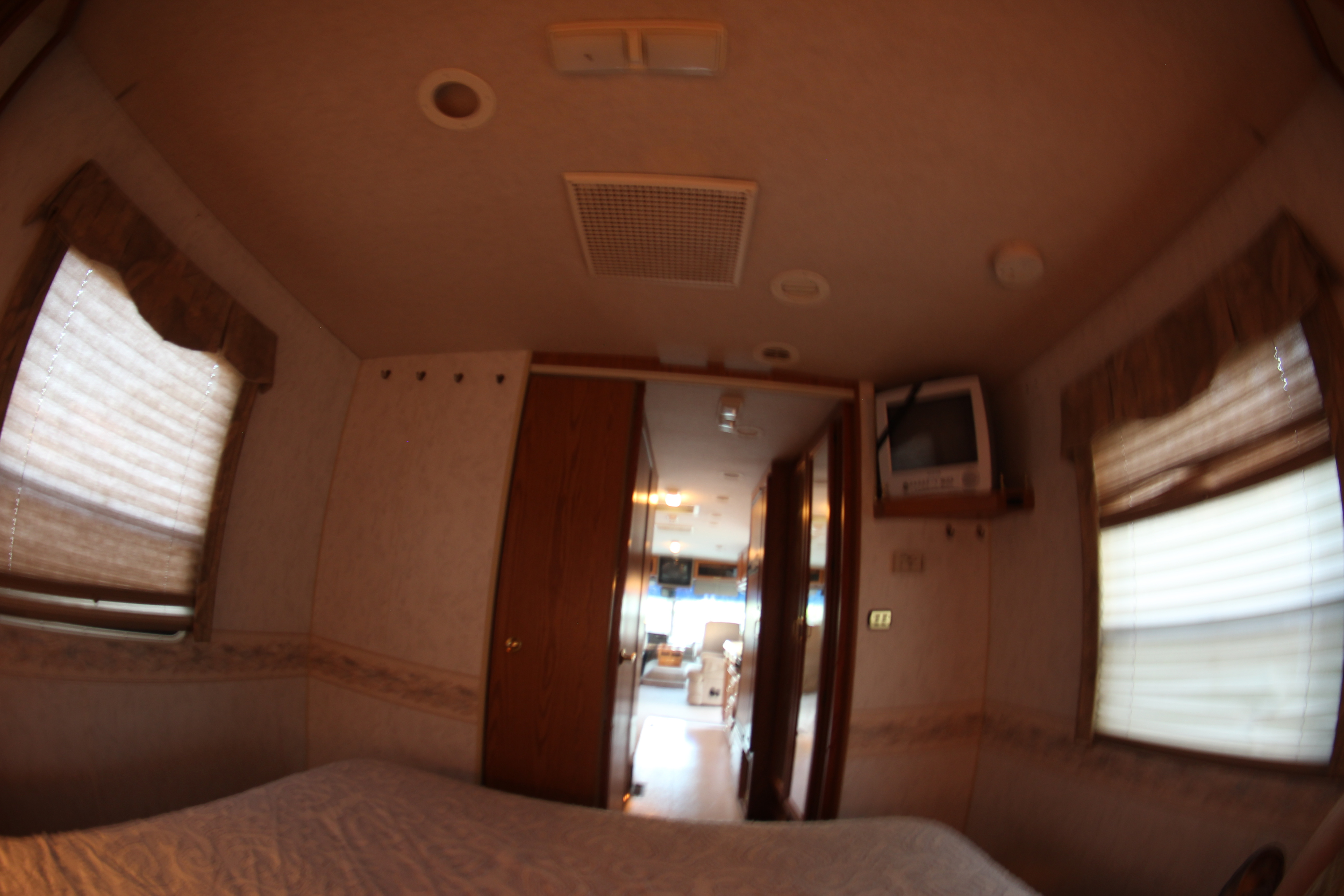 Cozy RV rental bedroom featuring a bed, window with blinds, and TV; a hallway leads to the living area.. Winnebago Adventurer 1999