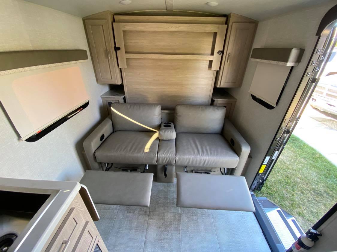 View inside an rv rental: reclining seats with footrests, a hidden wall bed, cabinets, and compact living amenities.. Forest River Rockwood 2021