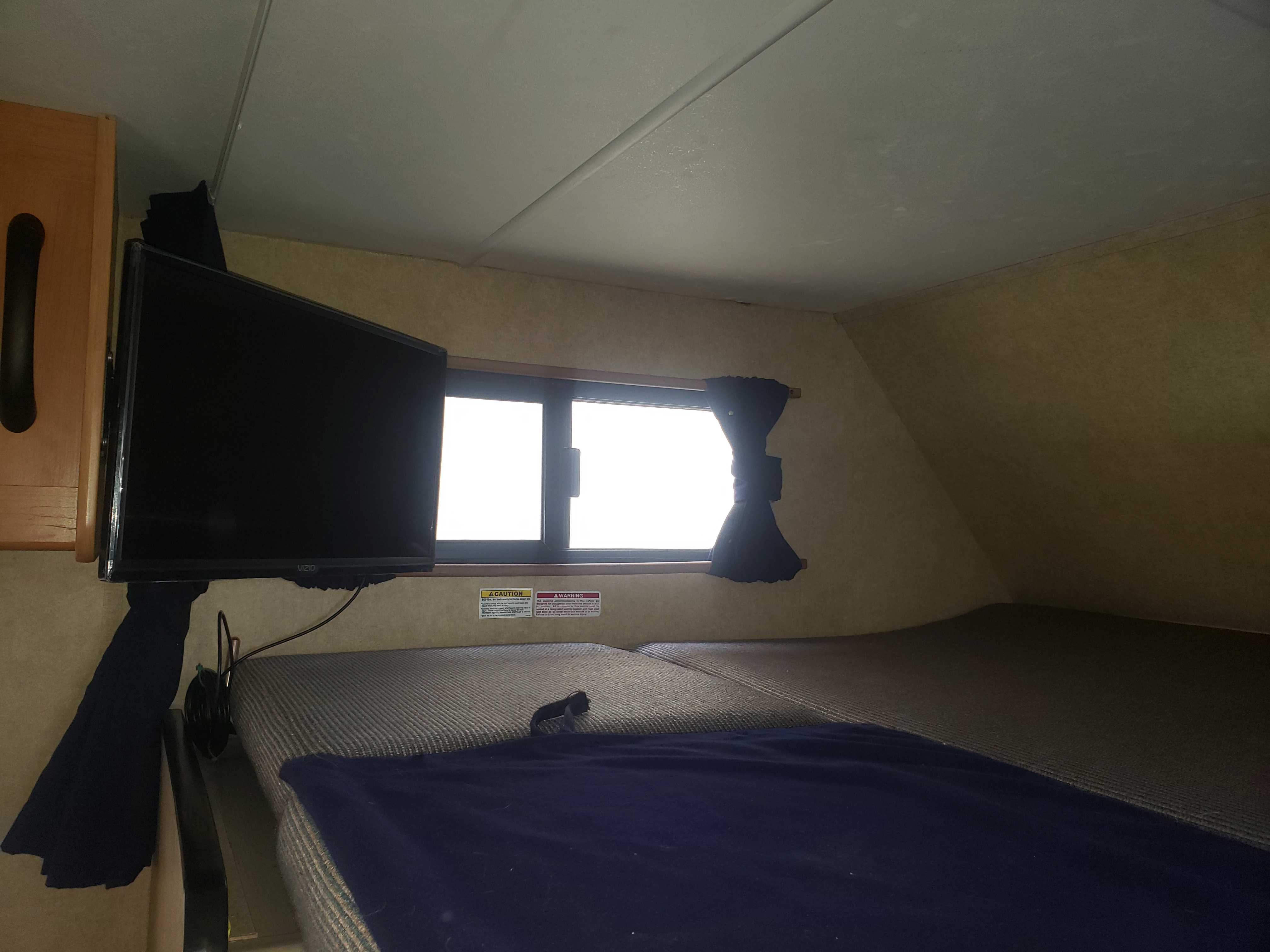 RV rental: A cozy sleeping area with a mounted TV, window, and comfortable bedding for your journey.. Thor Motor Coach Four Winds Majestic 2015