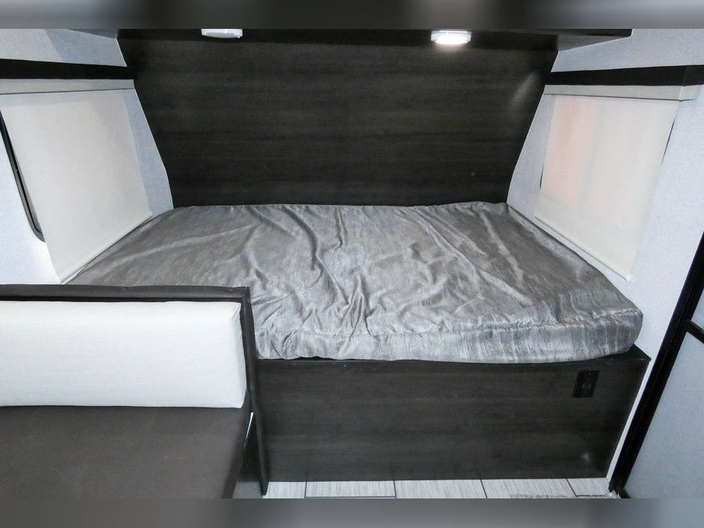 Cozy RV rental bedroom with a grey bed, dark wood accents, and white window blinds. Perfect for your next adventure!. Genesis Supreme Rv Surfside 2021