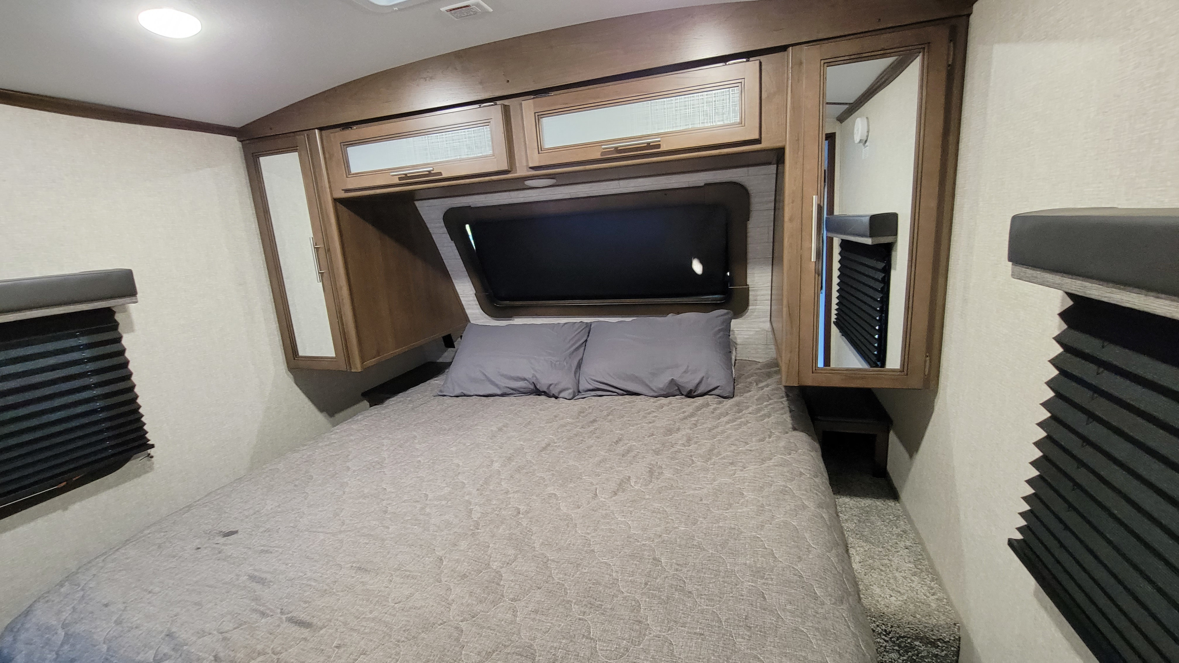 RV rental bedroom featuring a full bed, overhead cabinets, and mirrored wardrobes for comfortable travel.. Keystone Cougar Half-Ton 2020