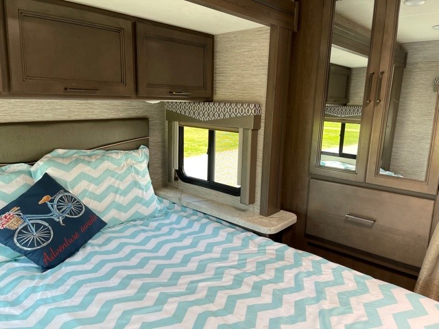 Cozy RV rental bedroom featuring chevron bedding, dark wood overhead cabinets, a window, and a mirrored closet.. Thor Motor Coach Freedom Elite 2021