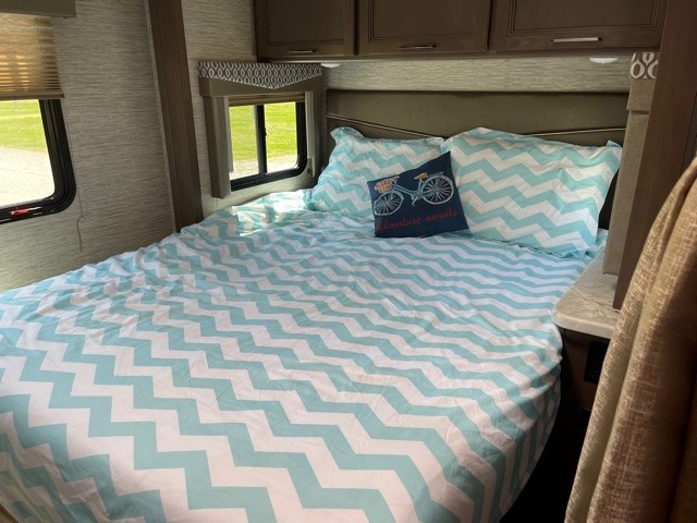Cozy RV rental bedroom featuring a bed with light blue chevron bedding, an "adventure" pillow, and scenic windows.. Thor Motor Coach Freedom Elite 2021