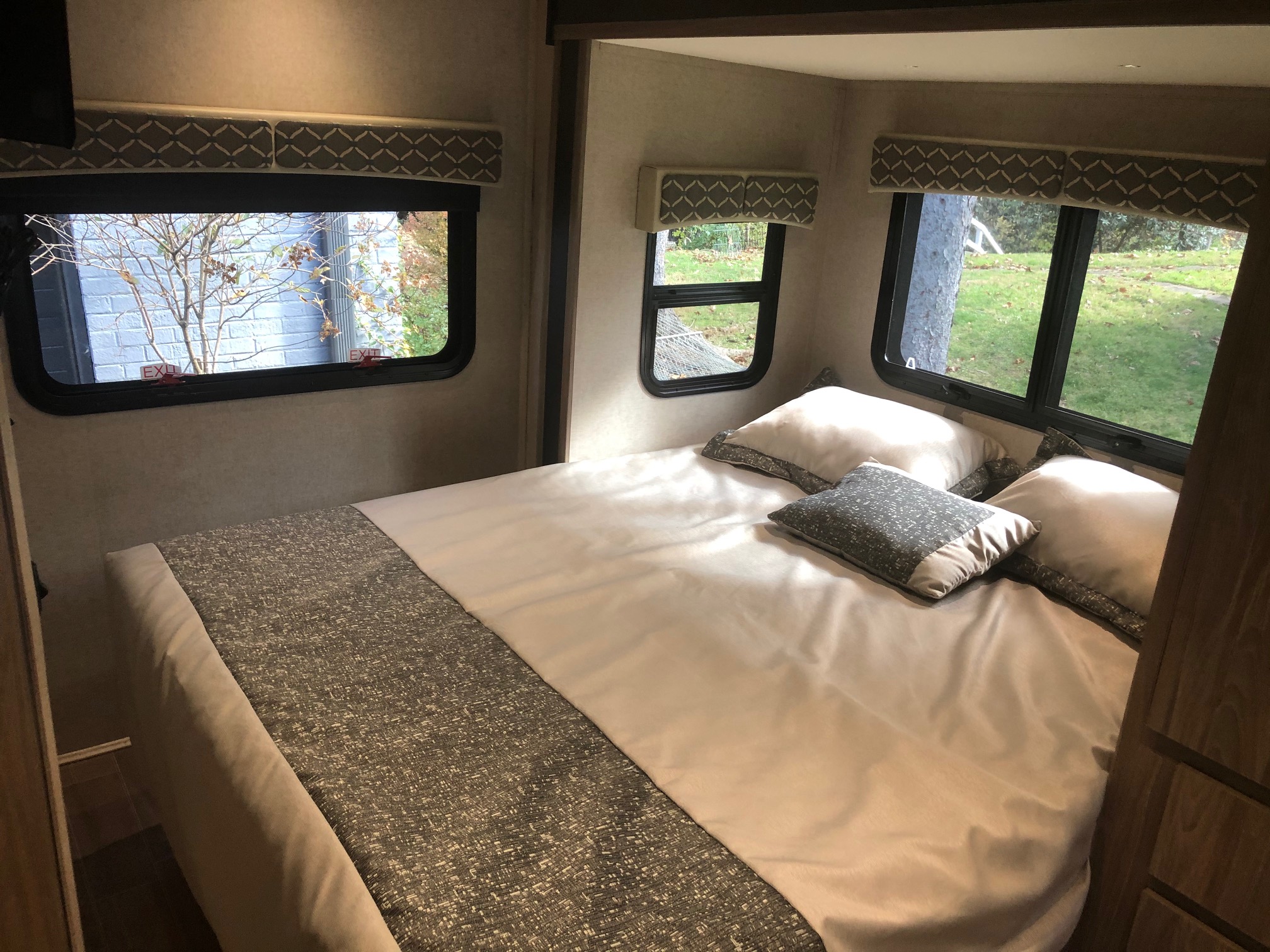 Bright RV rental bedroom: cozy bed, multiple windows with "EXIT" labels, and outdoor views. Great for travel.. Isata 3 2018
