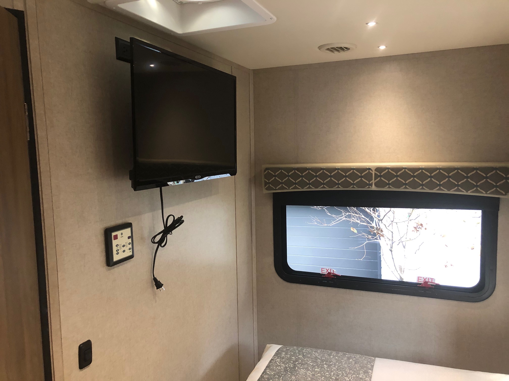 Inside an RV rental, a mounted TV, control panel, and window offer entertainment and views in this cozy bedroom space.. Isata 3 2018