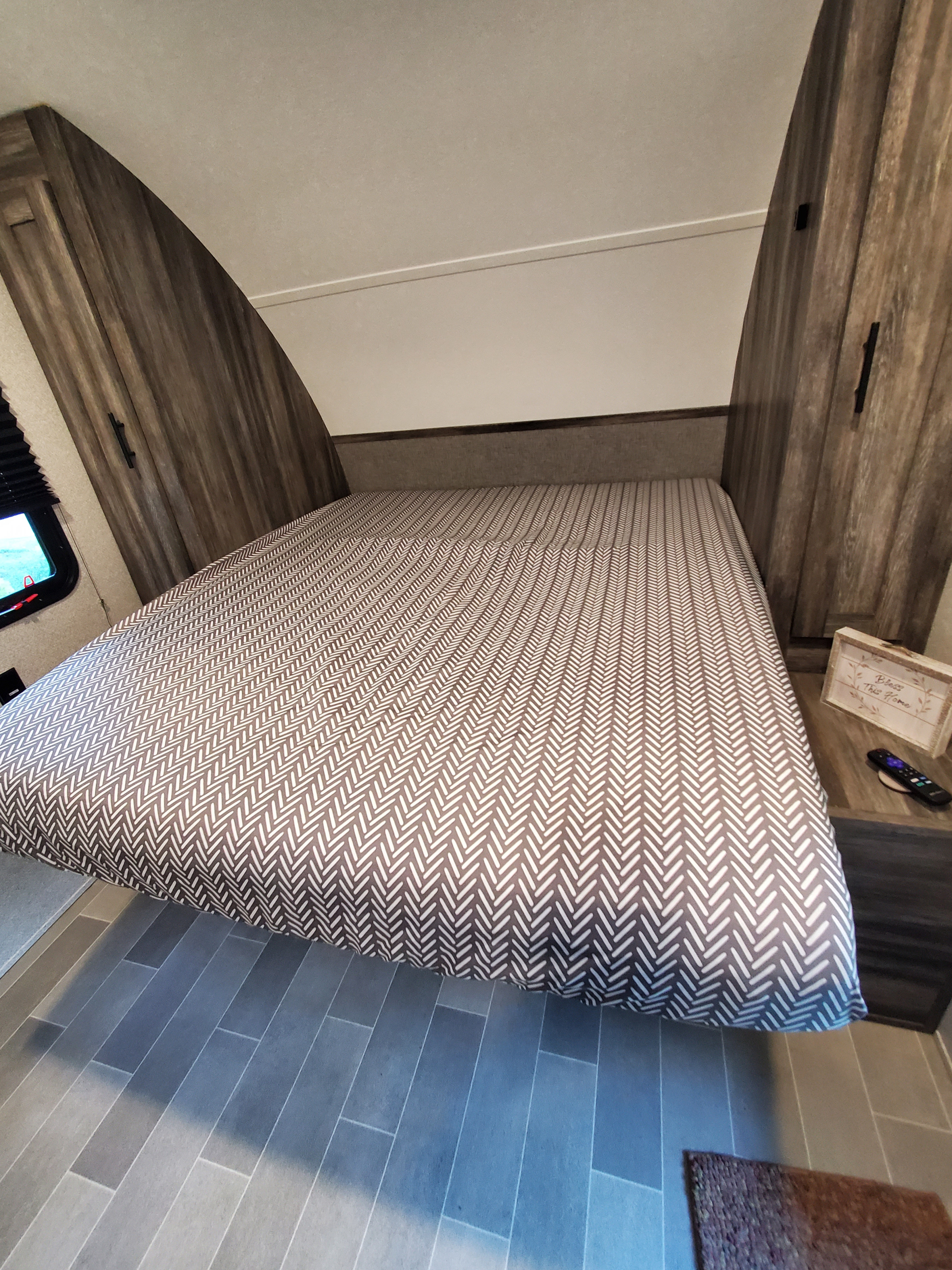 Cozy RV rental bedroom features a large bed with chevron comforter, wood cabinets, and grey plank floor.. Forest River Salem 2020