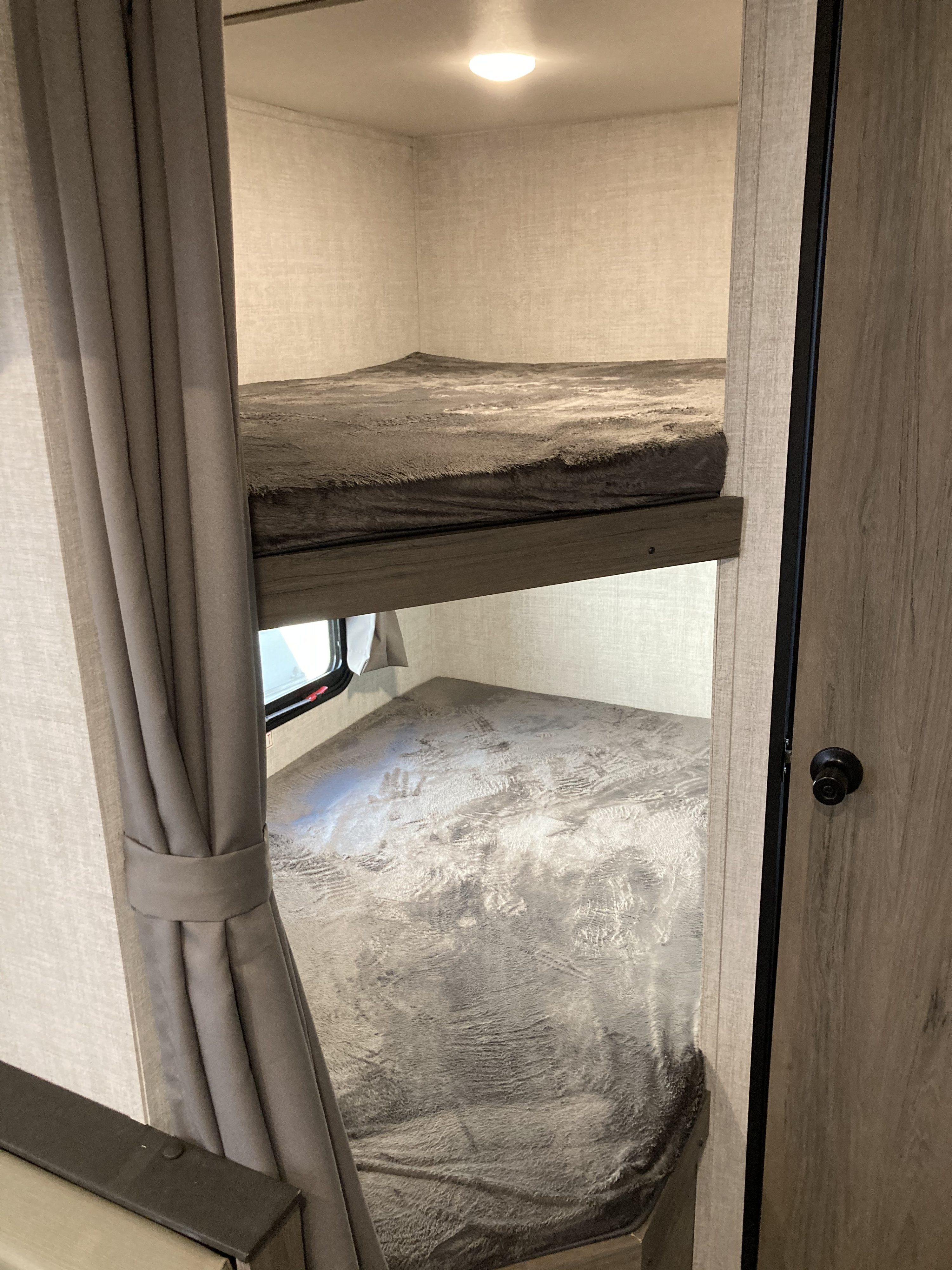 Inside an RV rental, two neatly made bunk beds with soft grey blankets offer a comfortable sleeping area.. Gulf Stream Conquest Lite 2021