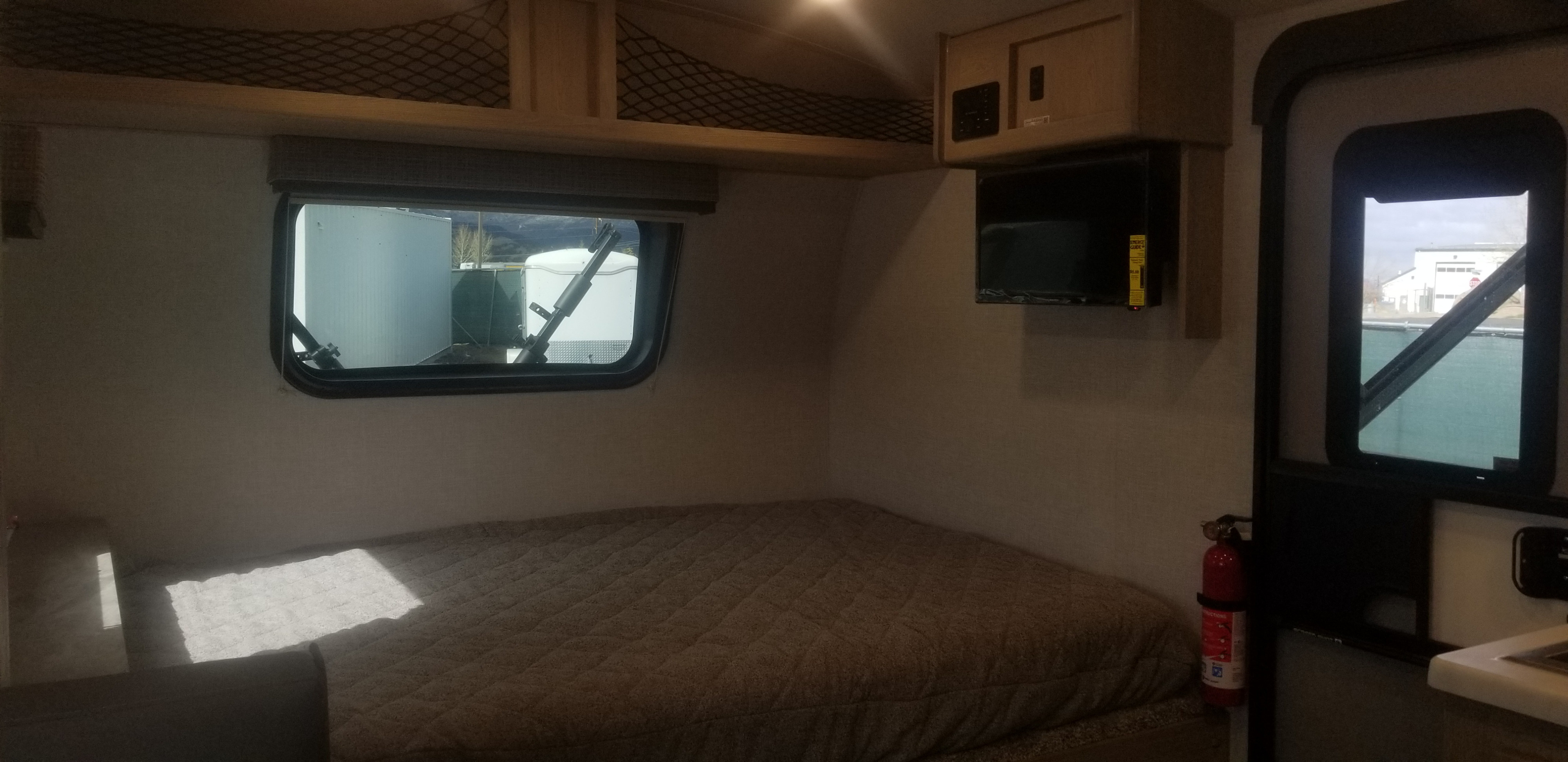 RV rental interior: cozy bedroom with quilted bed, window, overhead storage, mounted TV, and fire extinguisher.. Forest River Flagstaff 2021