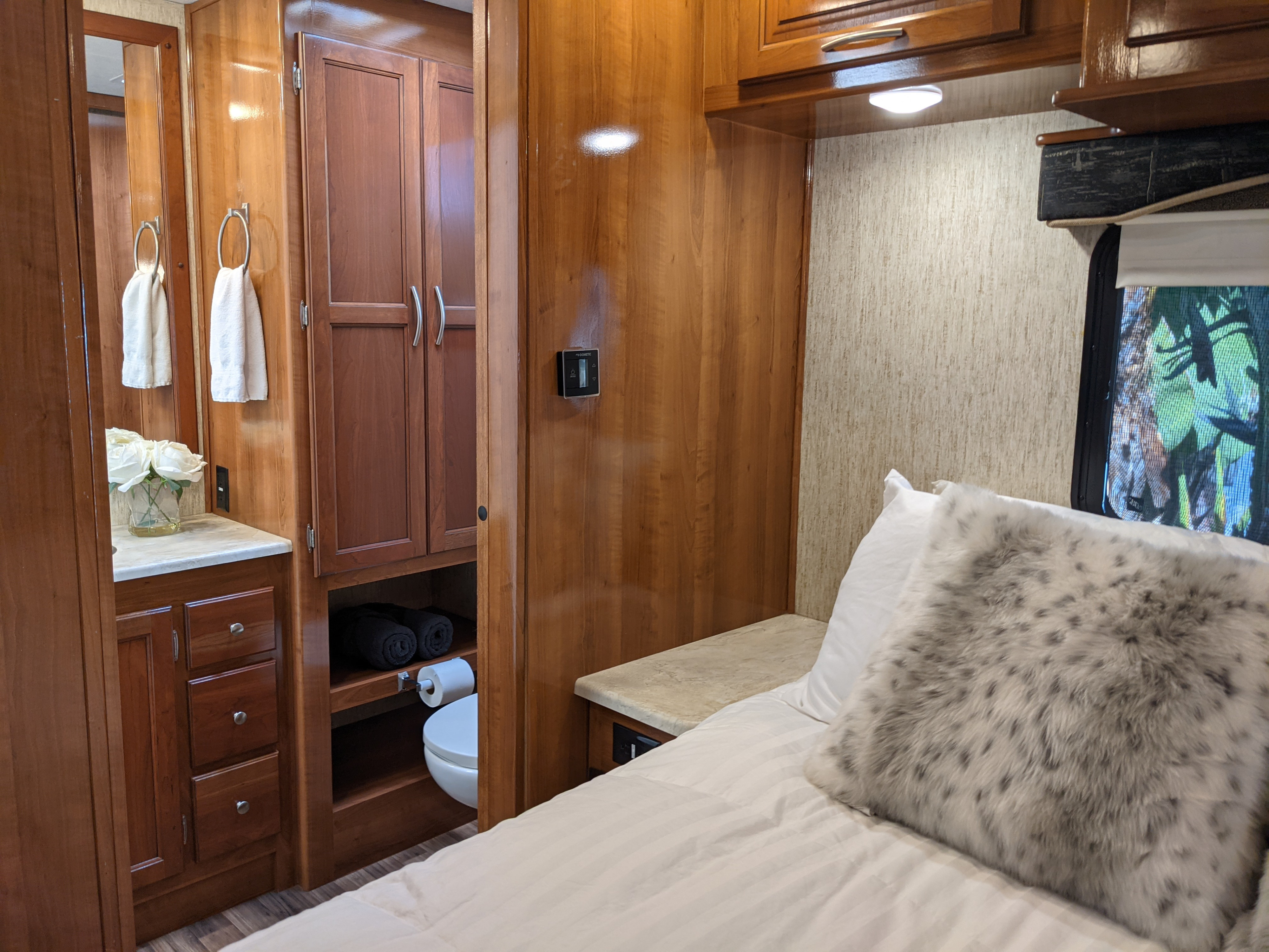 Cozy bedroom and compact bath area in a modern RV rental, featuring wood cabinetry and comfortable bedding.. Coachmen Mirada 2019